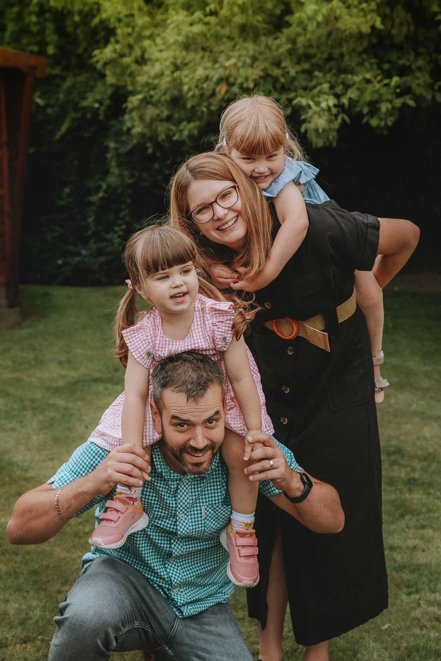 Playful family enjoying outdoor fun with children on shoulders in a backyard garden setting.