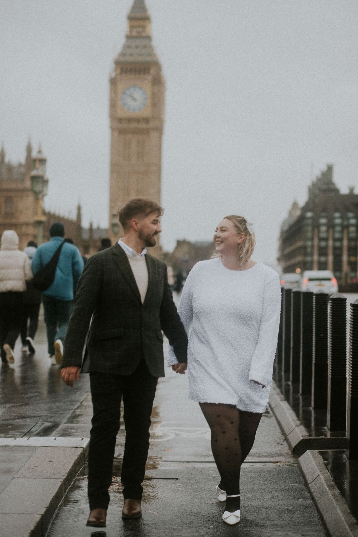 Couple walking along Thames River with Big Ben and London landmarks in background.