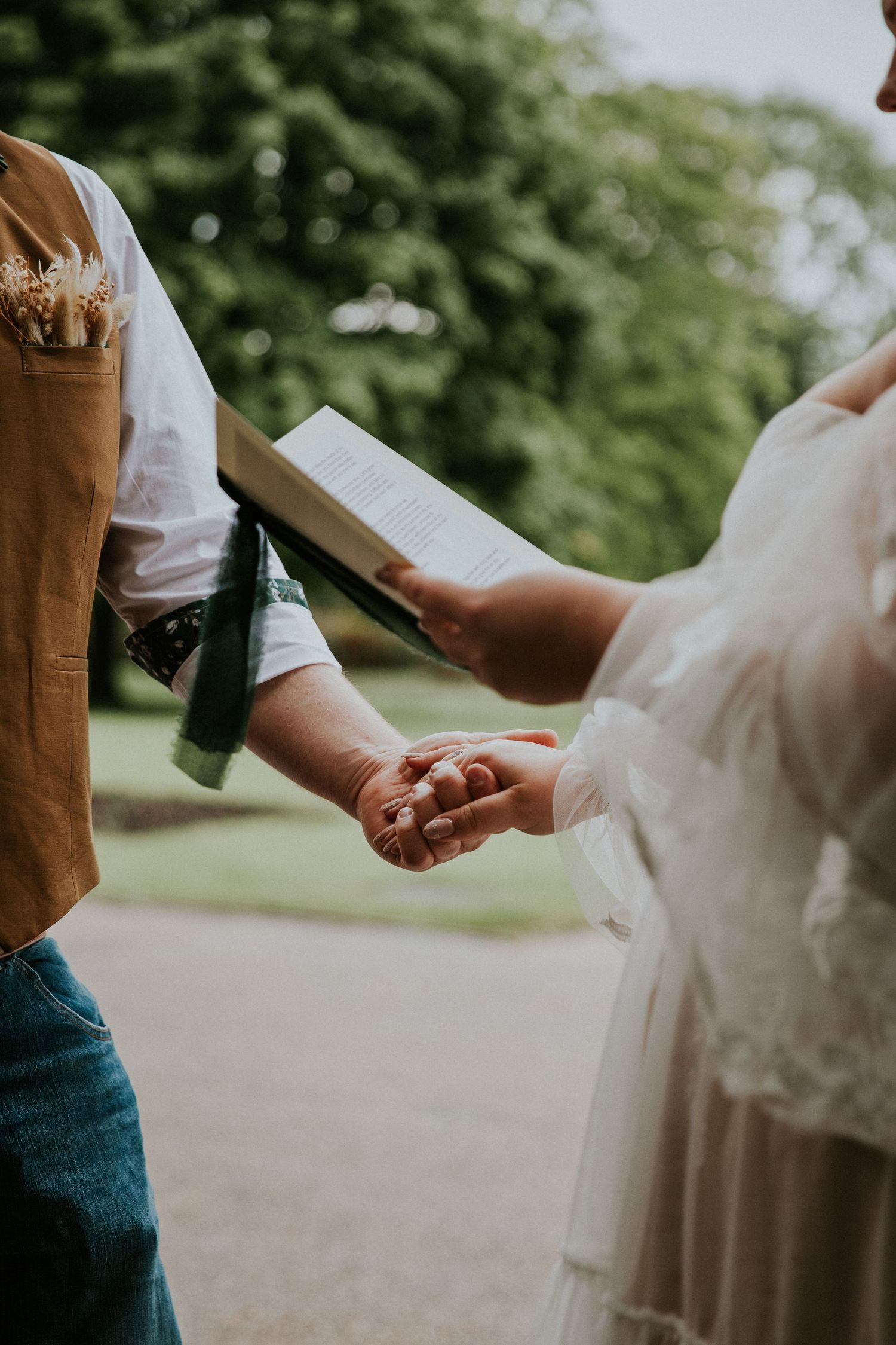 Close-up of couple holding hands during outdoor wedding ceremony while reading vows.