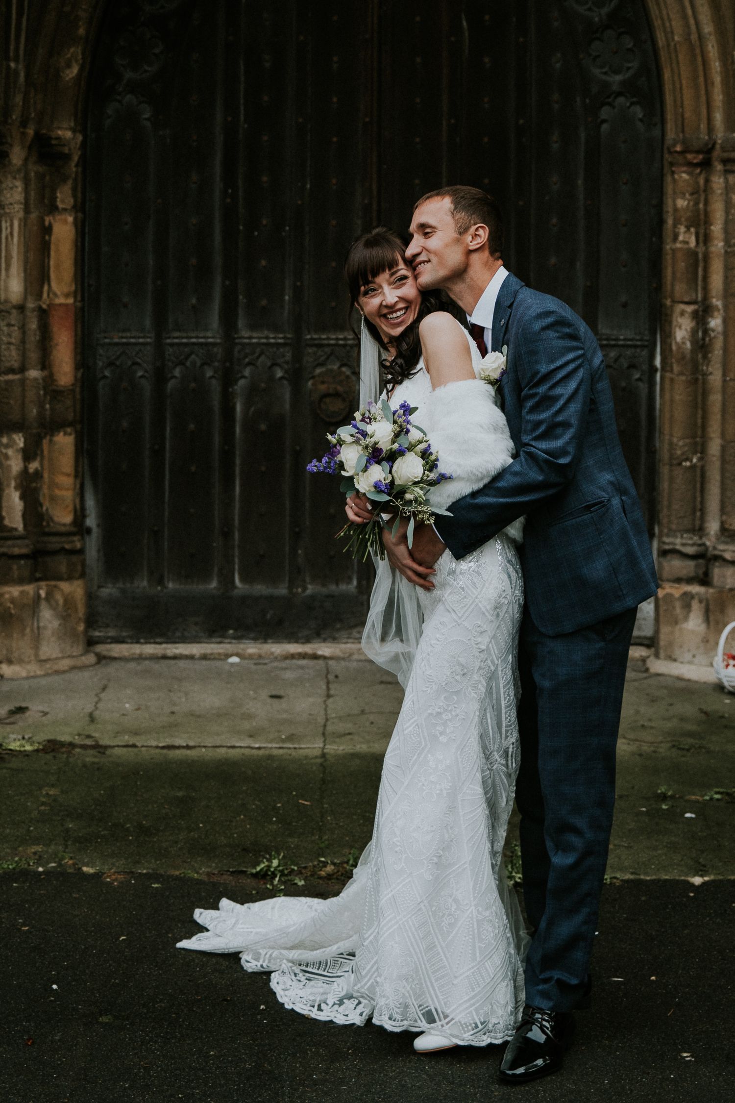 Romantic wedding couple poses in shadowy church archway with gothic architecture.