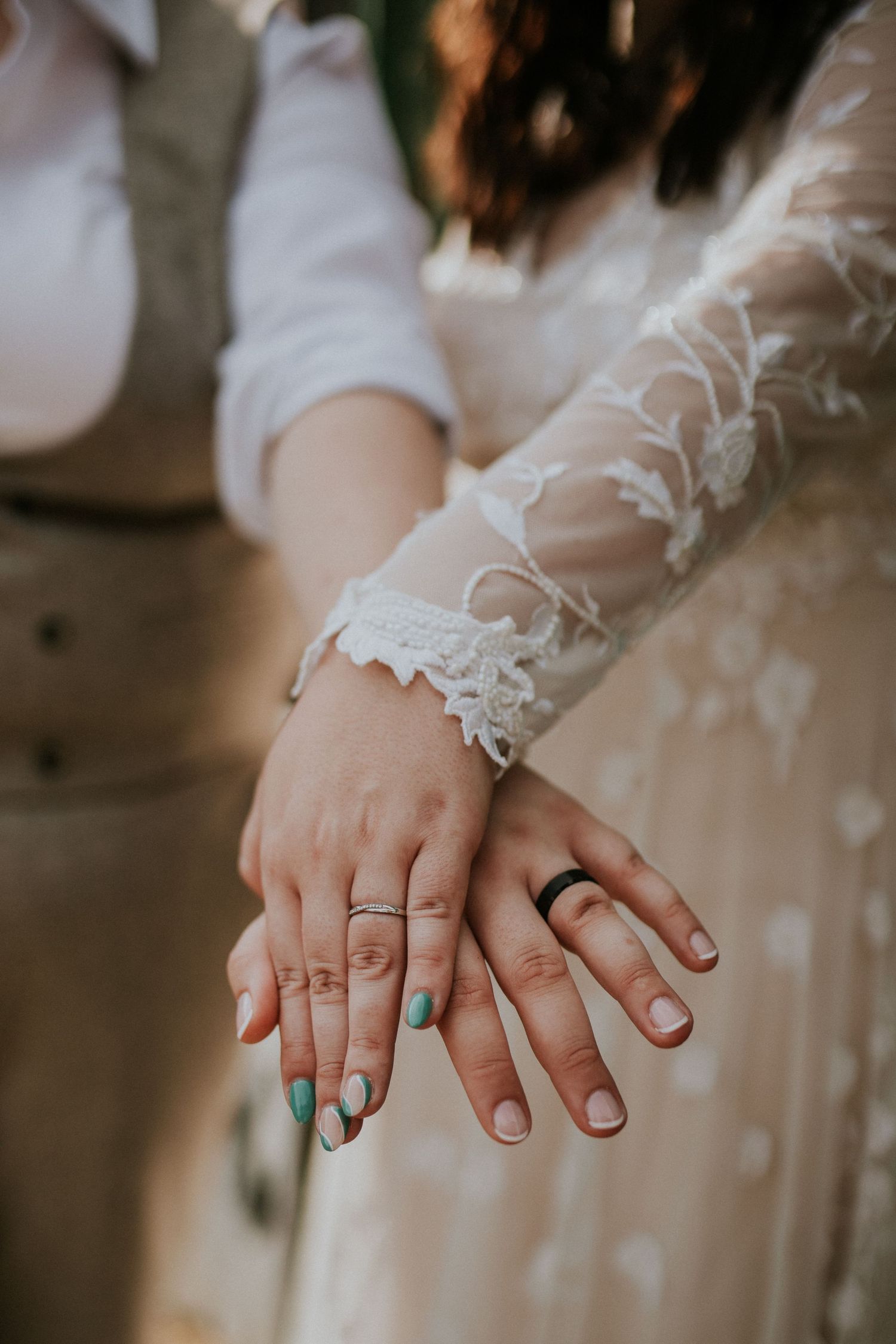 Close-up of hands showing wedding rings and turquoise nail polish against a lace sleeve detail.