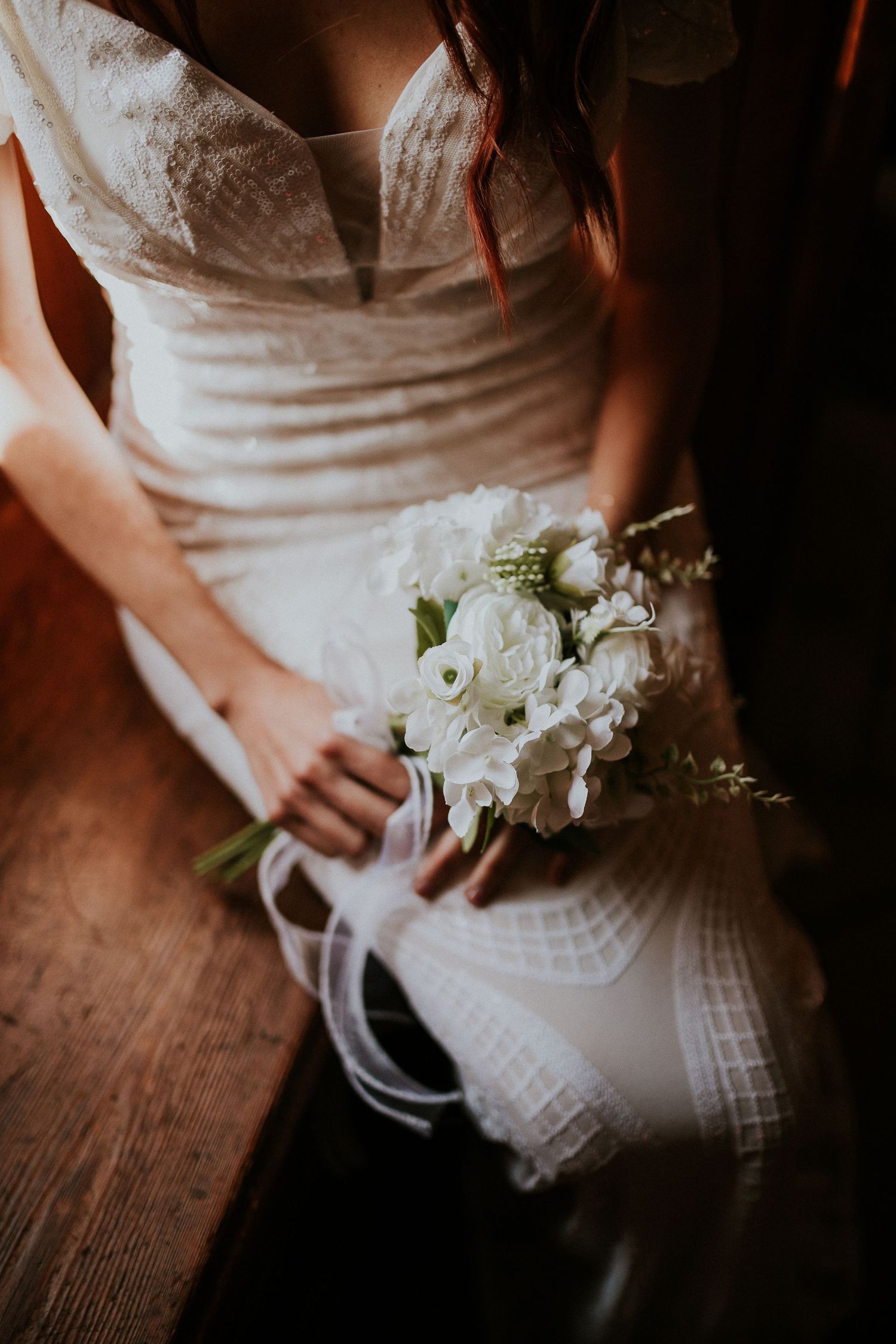 Close-up of bride holding delicate white floral bouquet with flowing ribbons.