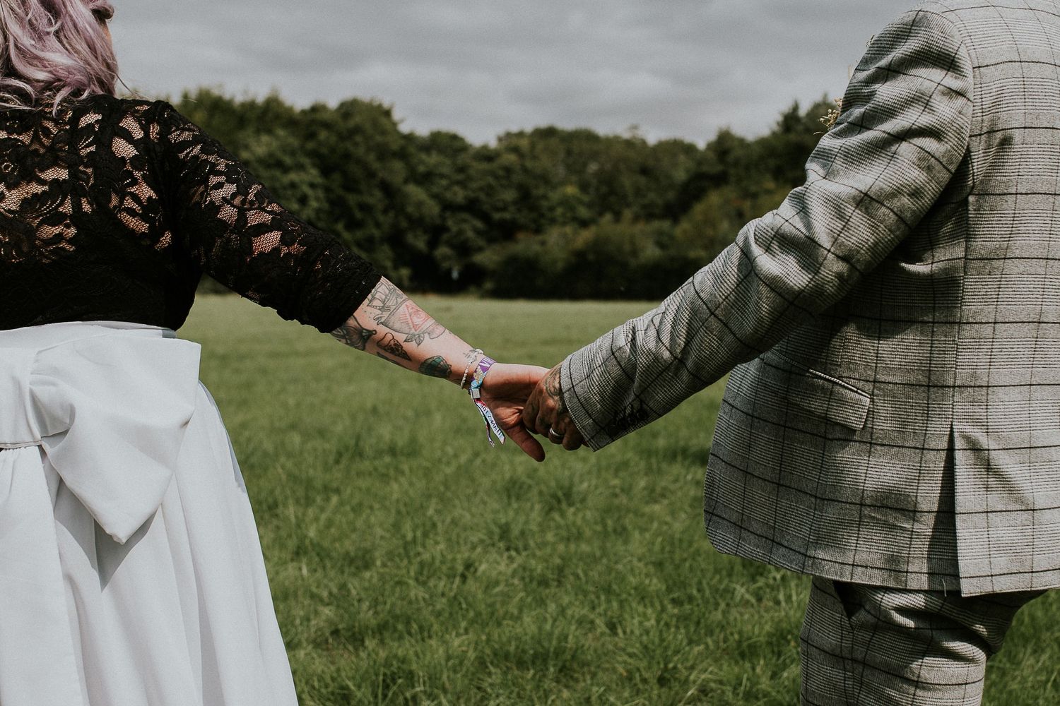 Close-up of couple holding hands with wedding attire visible in a green field.
