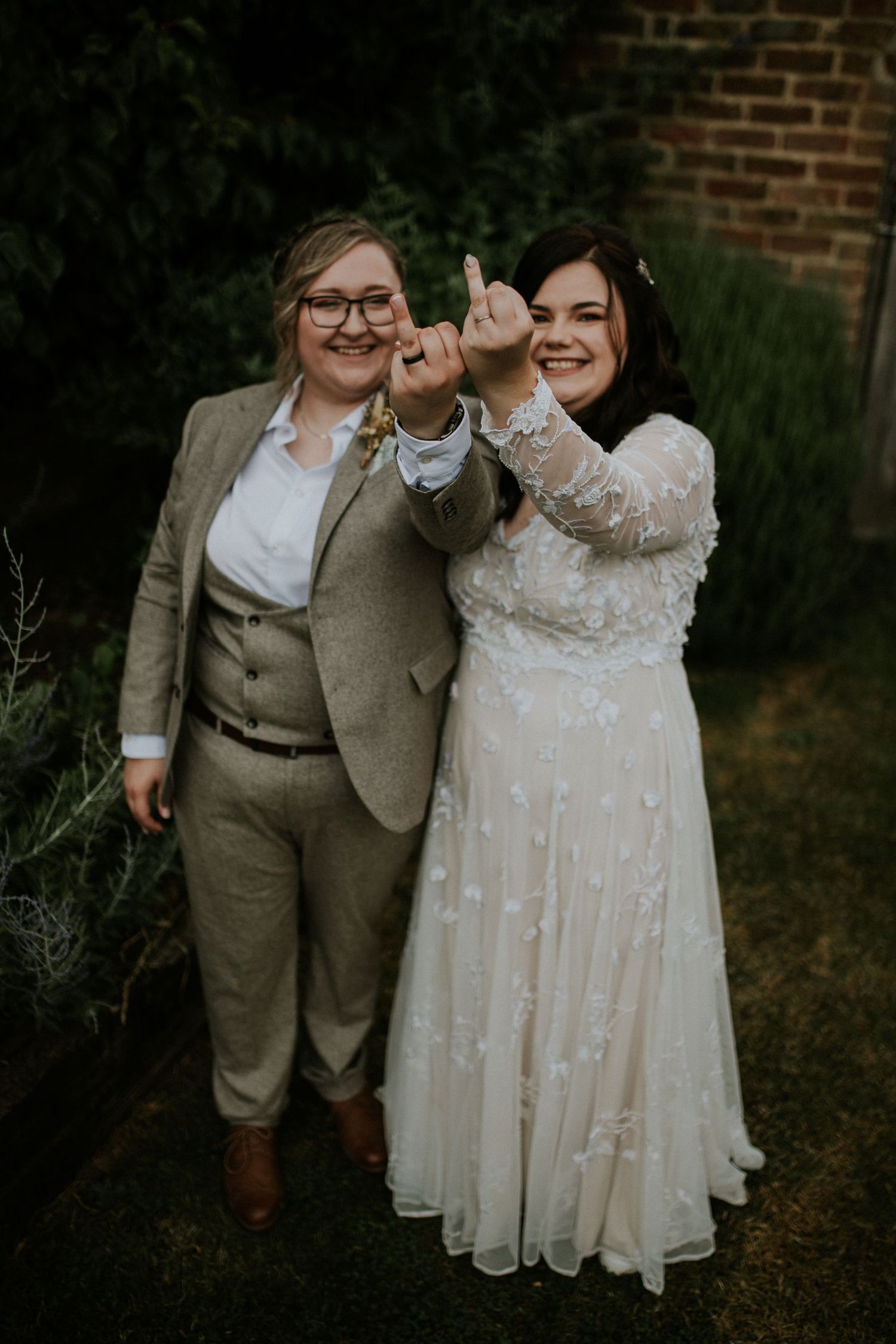 Wedding celebration in front of a brick wall with couples wearing white dress and beige suit.