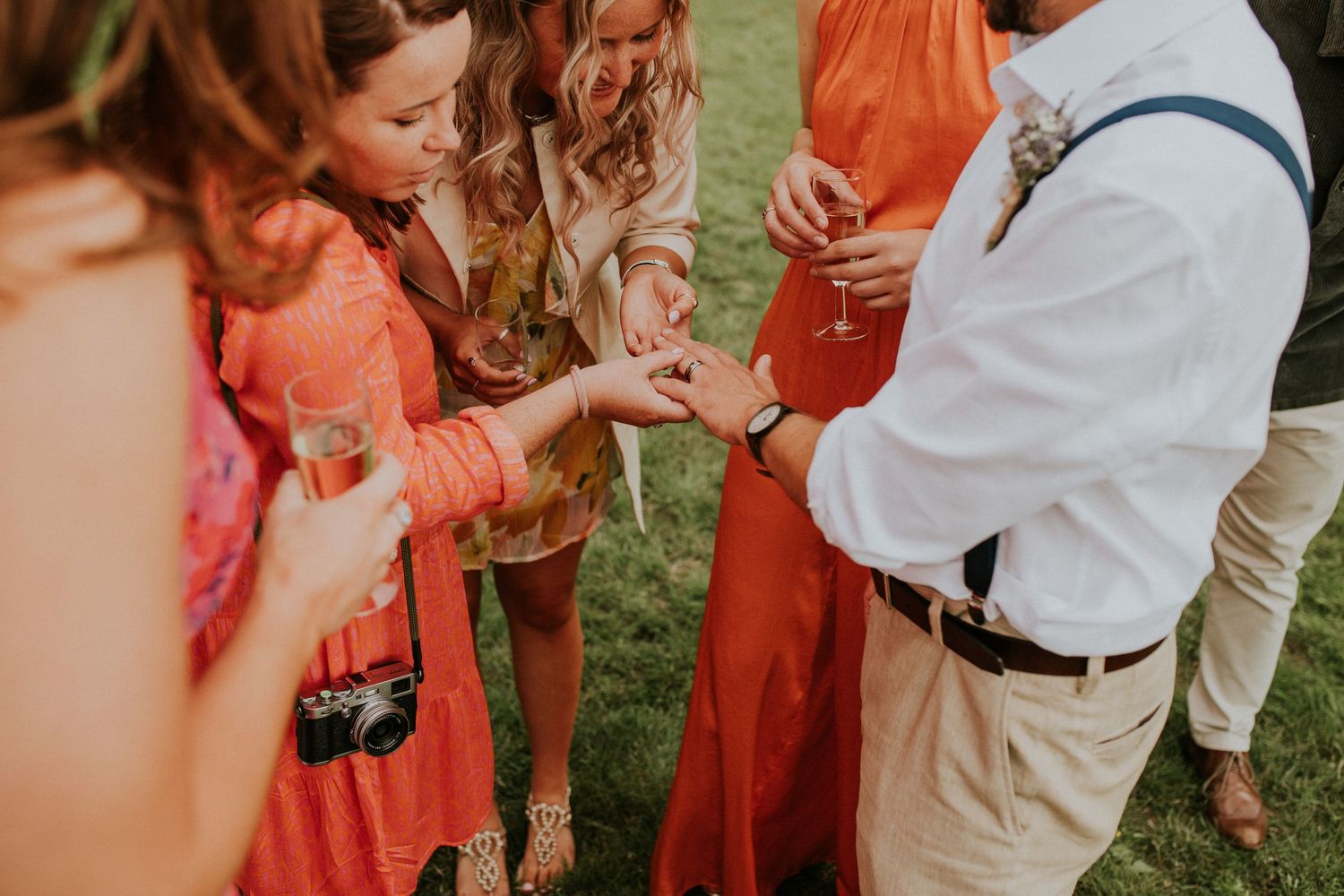 Wedding guests dance and celebrate at an outdoor reception wearing coral-colored dresses and formal attire.