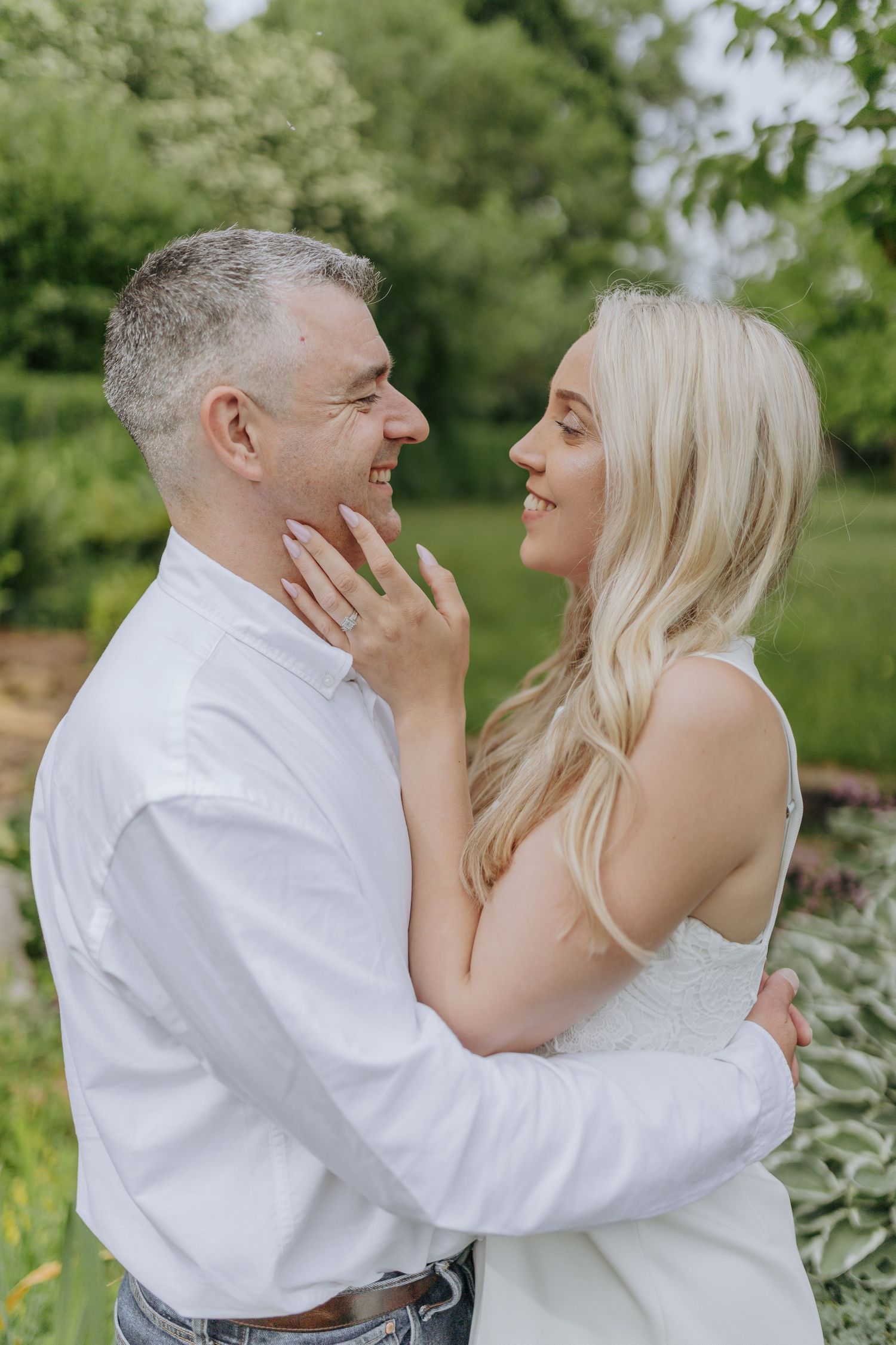 A couple shares playful and joyful moments outdoors in a garden setting with lush greenery in the background.