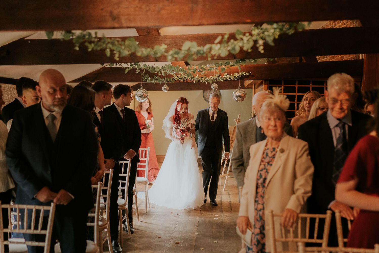 Wedding ceremony processional in a rustic indoor venue with natural lighting.