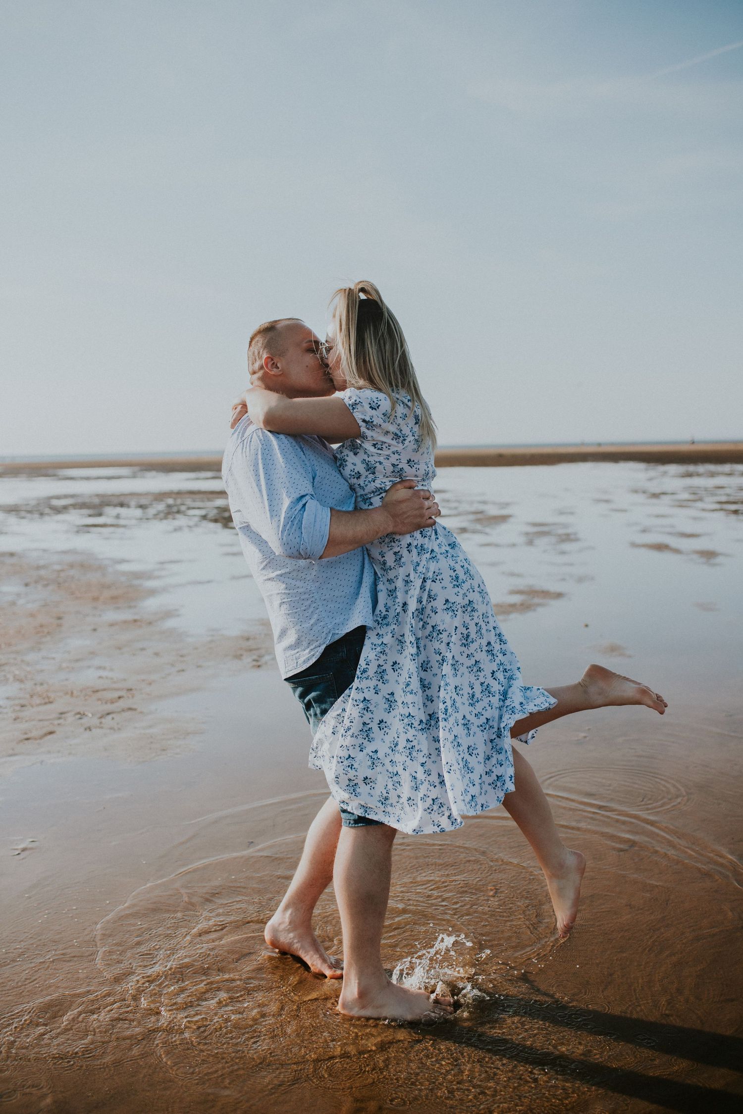 A joyful couple embraces and shares a romantic moment together on a sandy beach at sunset.
