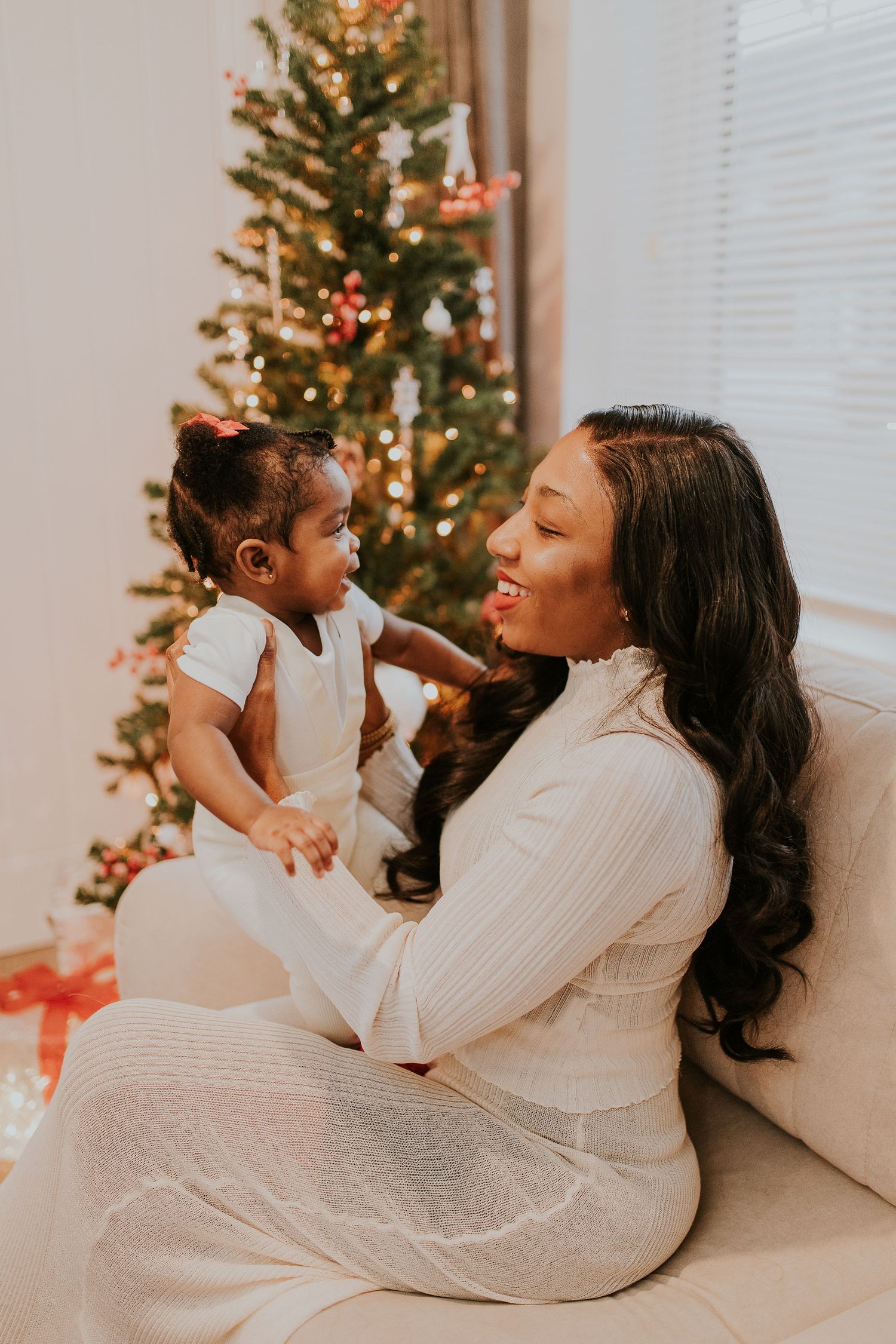 Mother and child share tender holiday moments by decorated Christmas tree in white sweaters.
