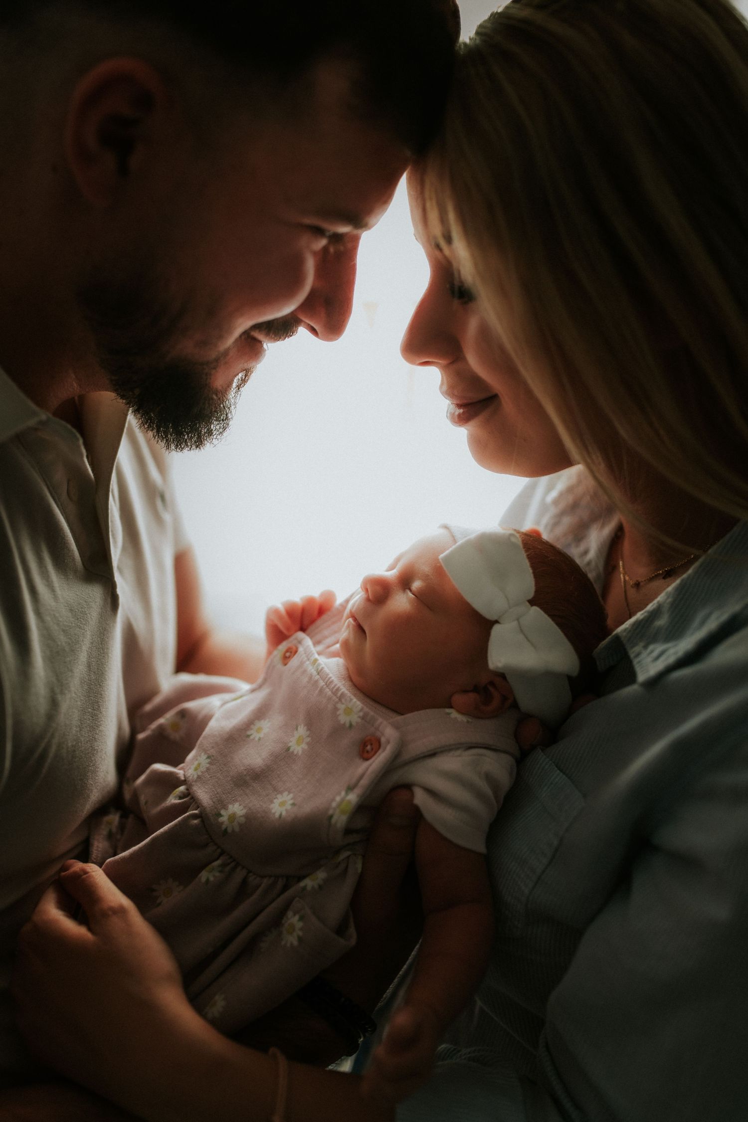 Intimate family moment with newborn baby captured in soft, moody lighting.