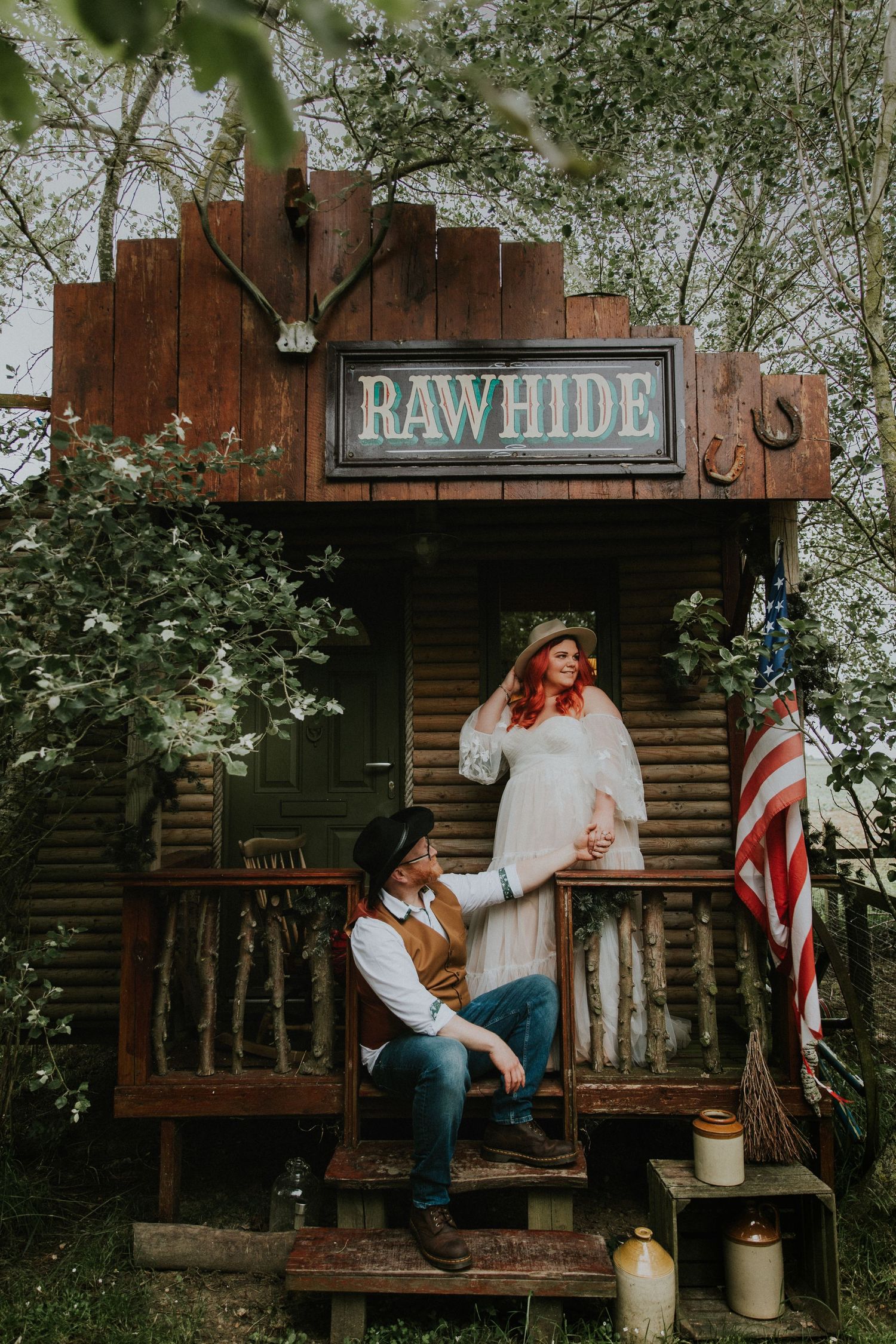 Rustic outdoor photoshoot in front of a wooden cabin with Rawhide sign.