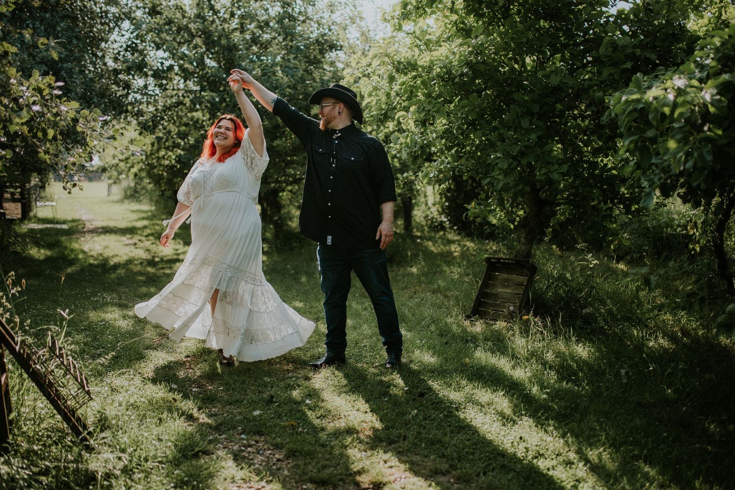 Couple in wedding attire dancing joyfully in sunlit garden.