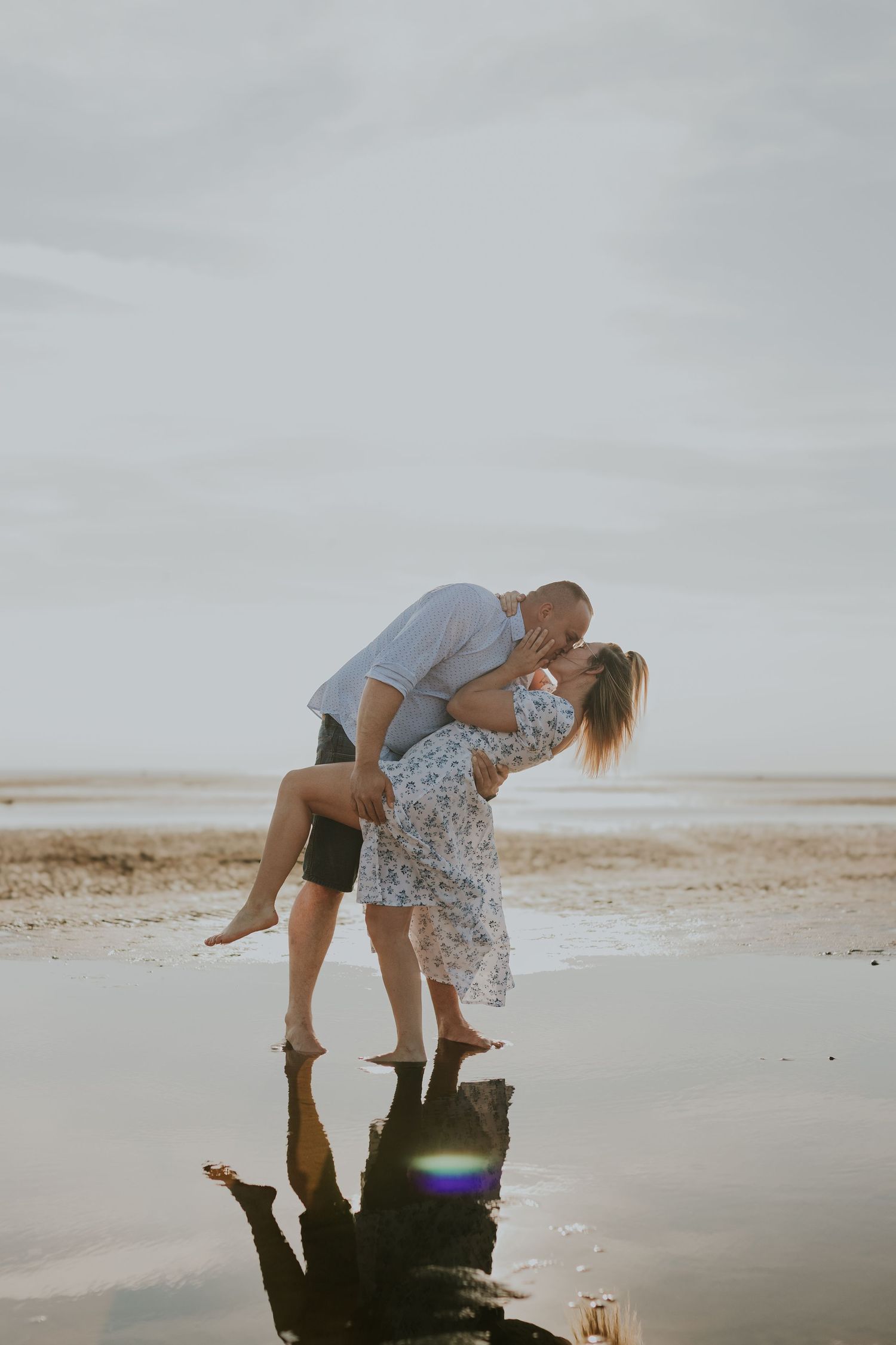 Couple shares romantic dip pose on reflective beach at sunset.
