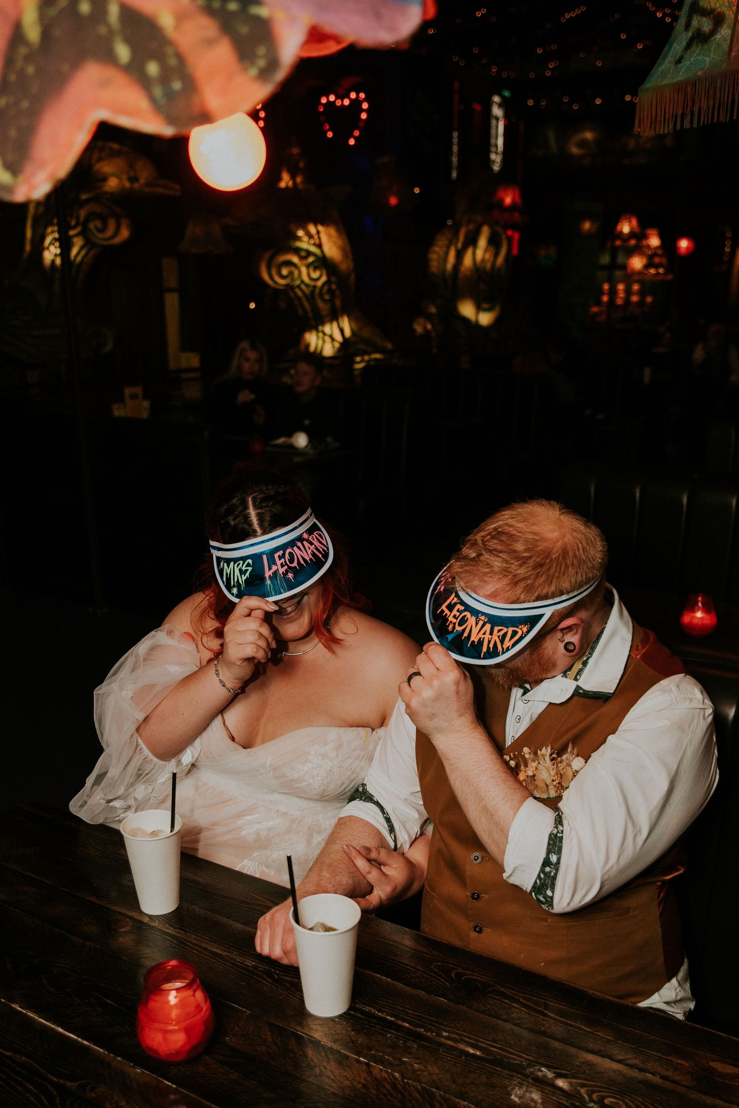 Couple wearing matching party visors sharing a fun moment at their reception.