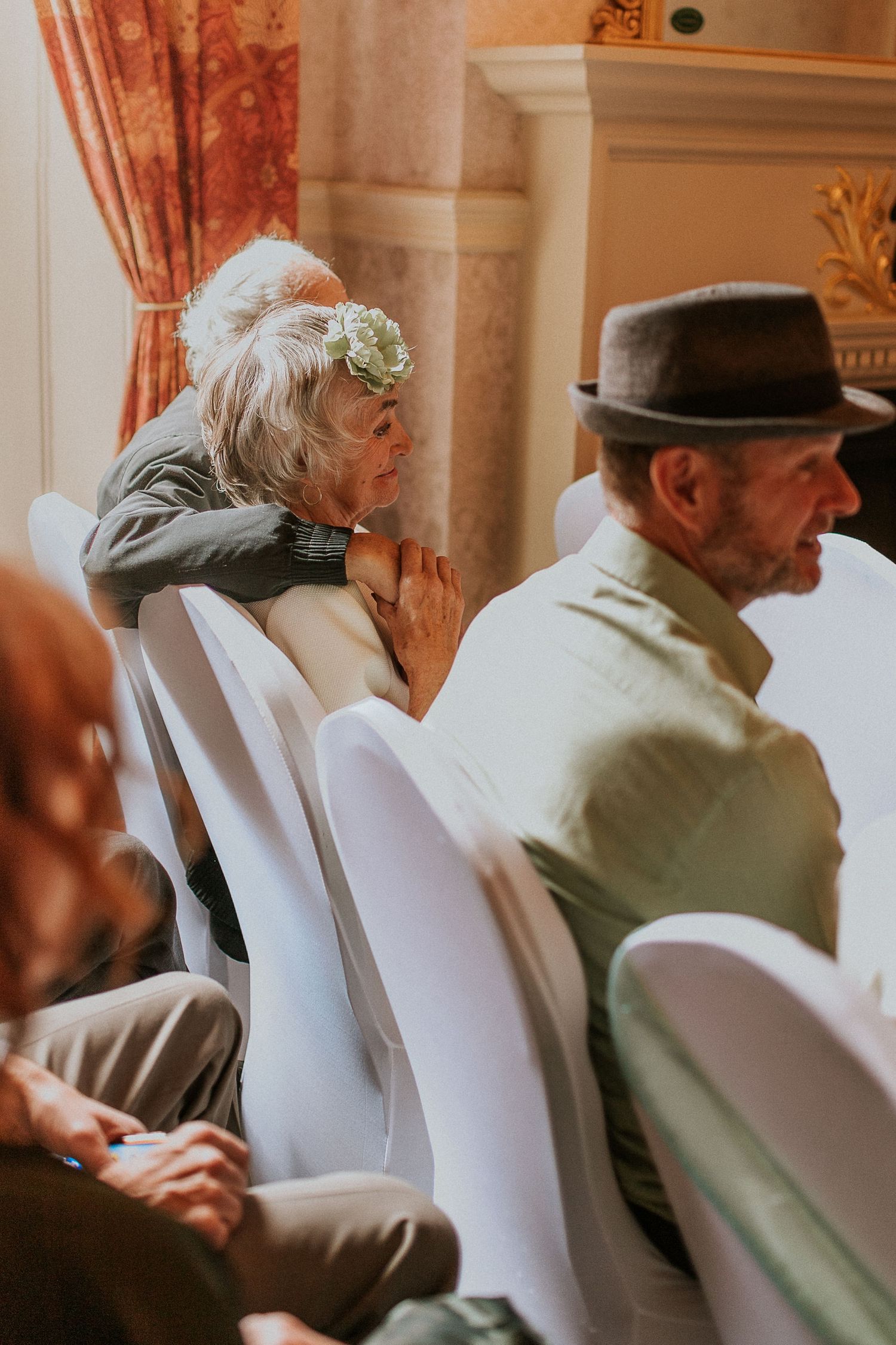 Wedding guest in elegant attire seated at an indoor venue with ornate decor.