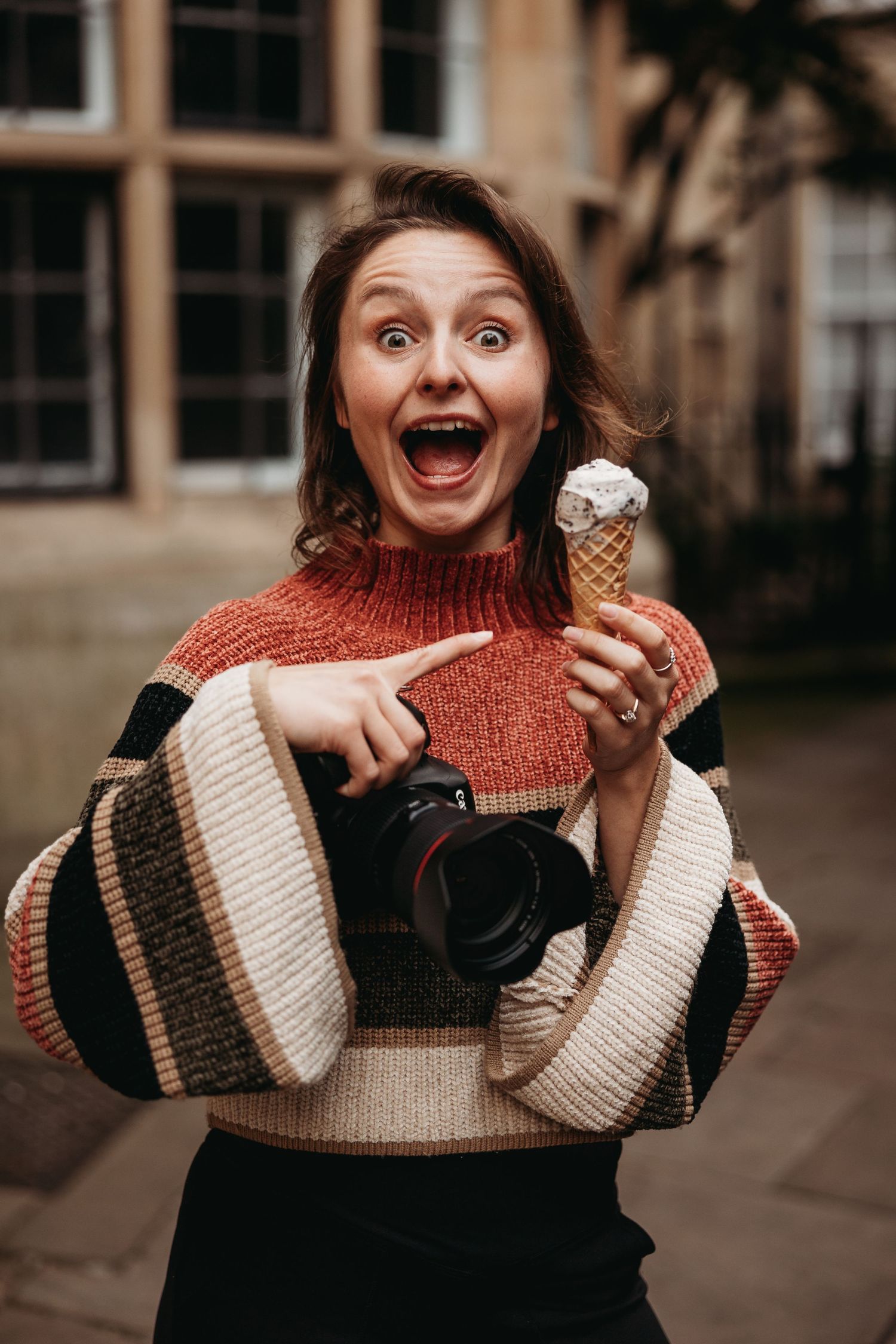 Excited photographer pointing at ice cream cone while holding camera and wearing striped sweater.