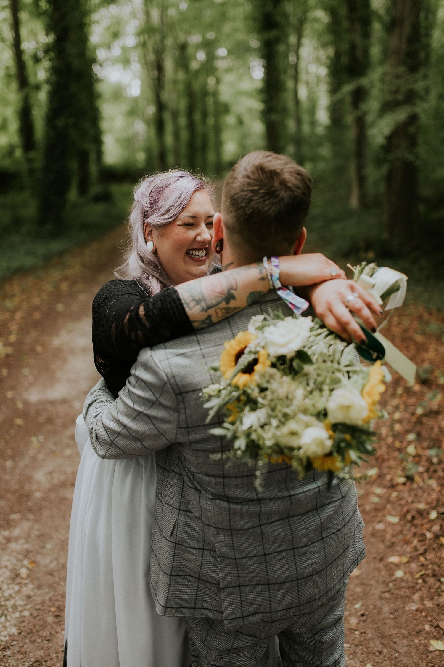 Joyful couple embracing on forest path with sunflower bouquet during wedding celebration.
