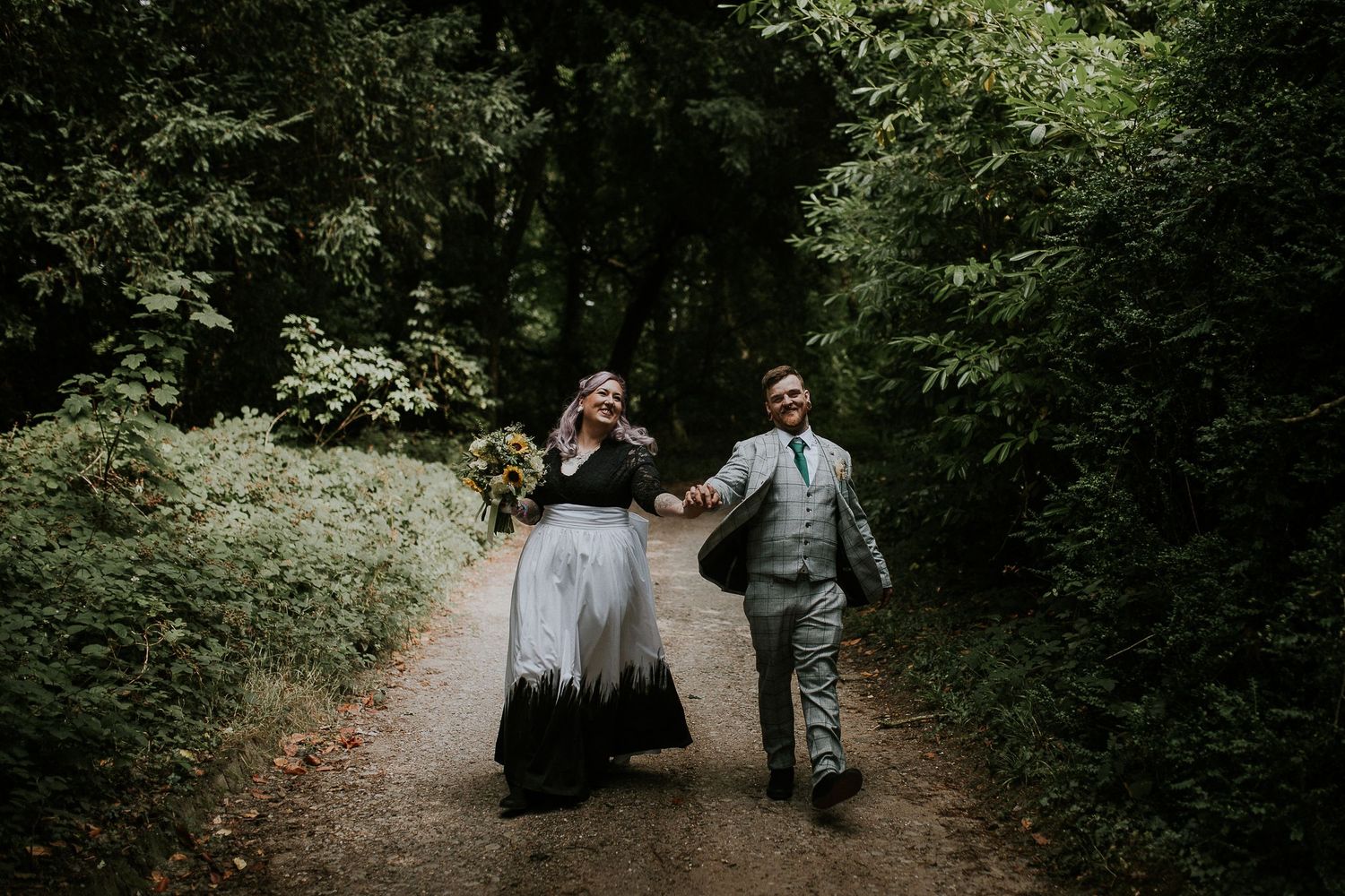 Couple walks joyfully on a forest path during their wedding celebration.