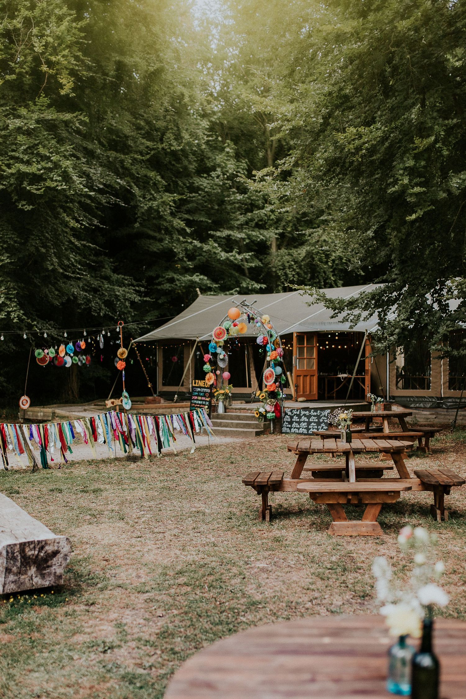 Rustic outdoor wedding venue with wooden cabin and colorful balloon decorations in a forest setting.