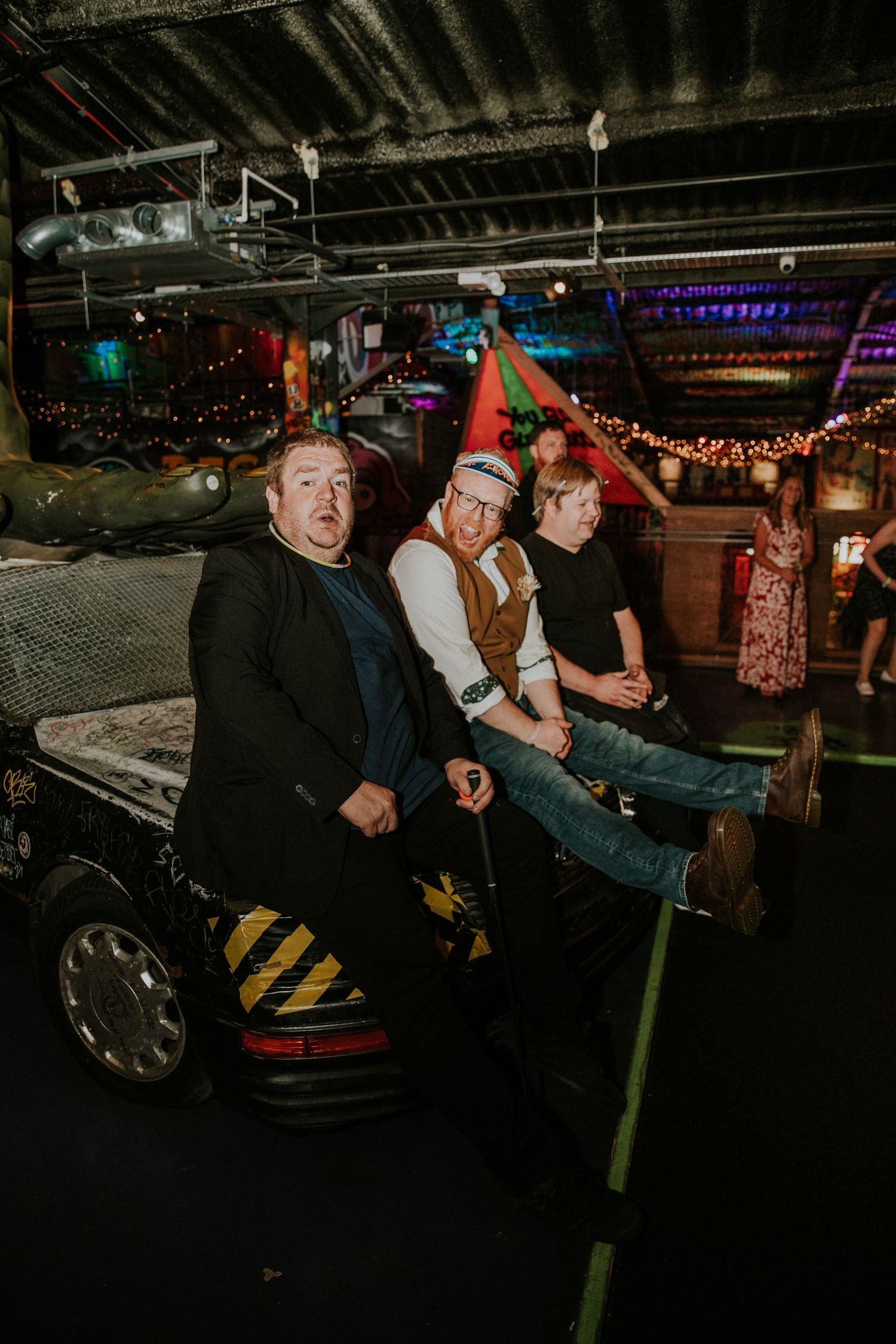 Wedding party riding in vintage car at night with colorful venue lighting.