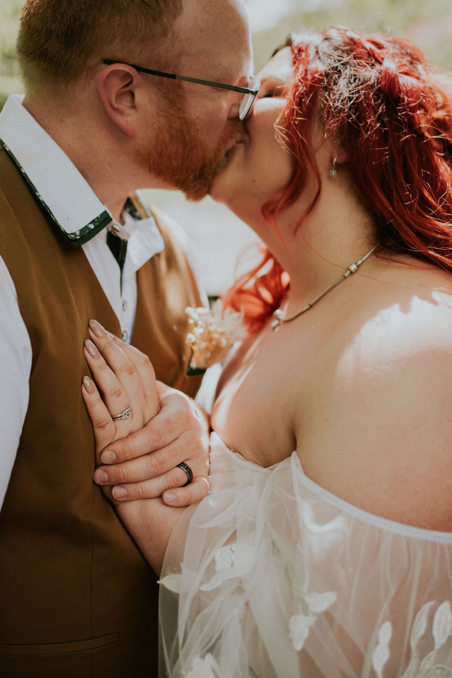 Intimate moment of newlyweds sharing their first kiss, groom in brown vest and bride in white dress.