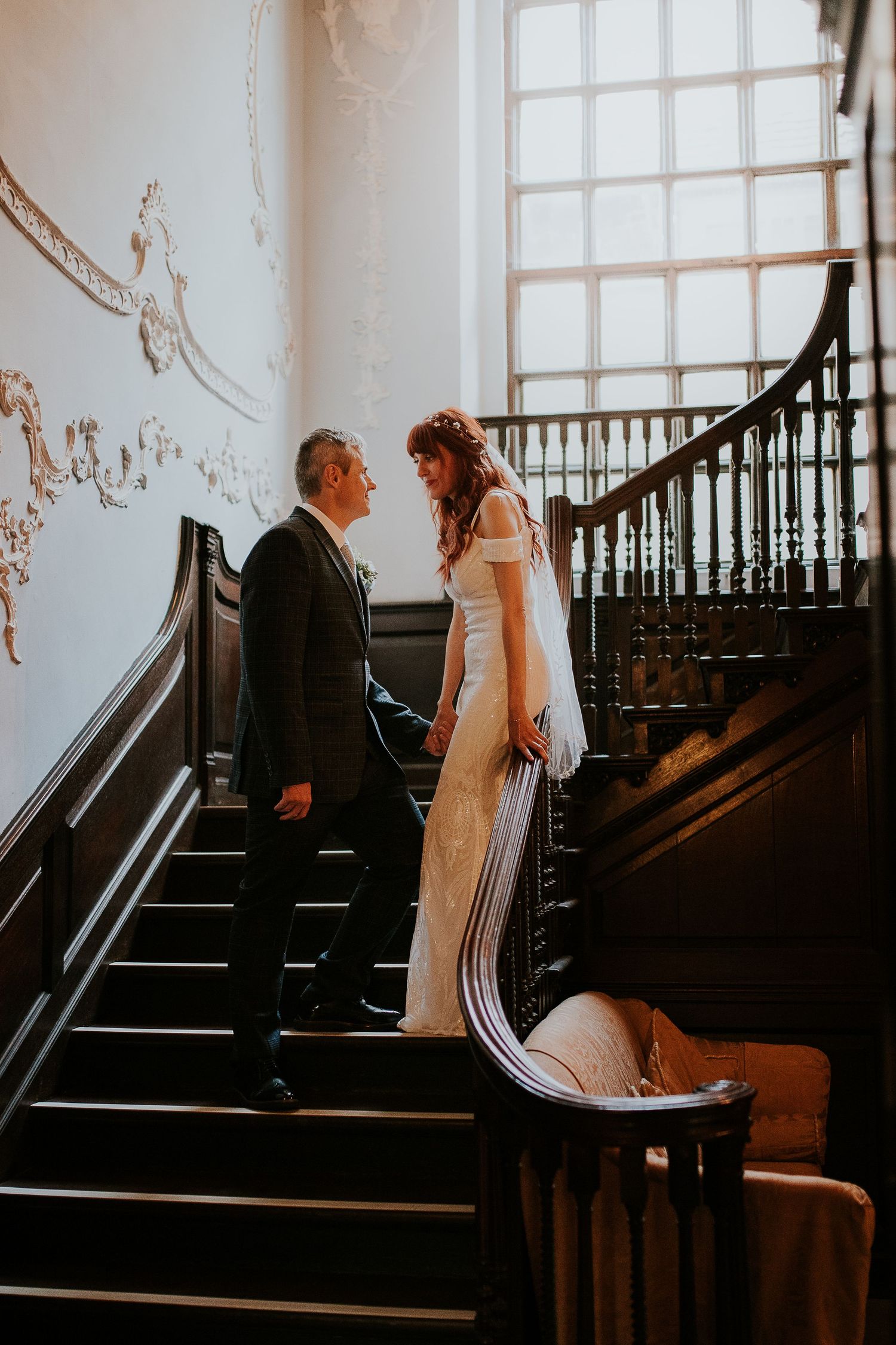 Wedding couple sharing romantic moments on an elegant staircase with natural window lighting.