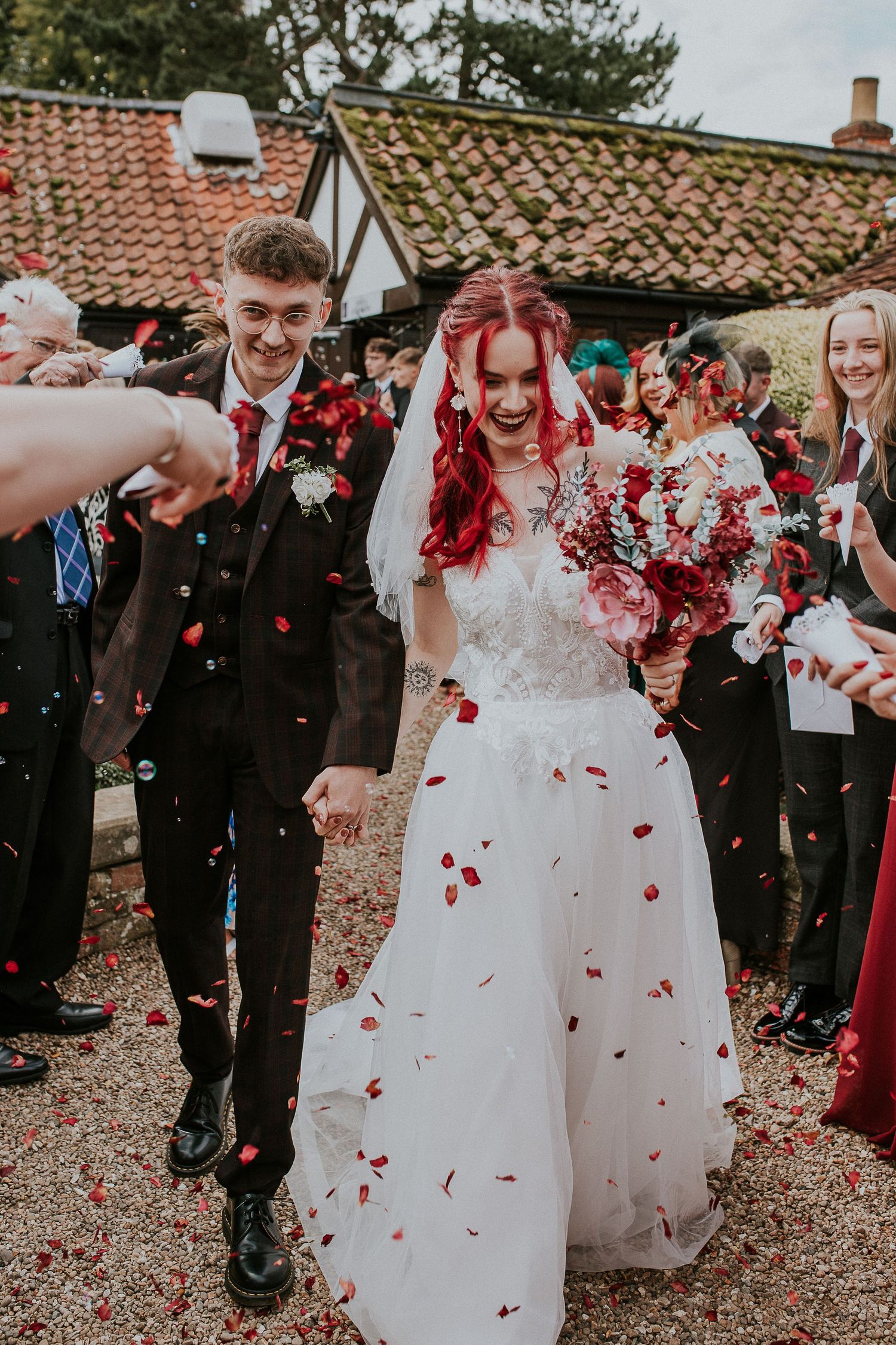Newlyweds walking through shower of red rose petals after wedding ceremony.