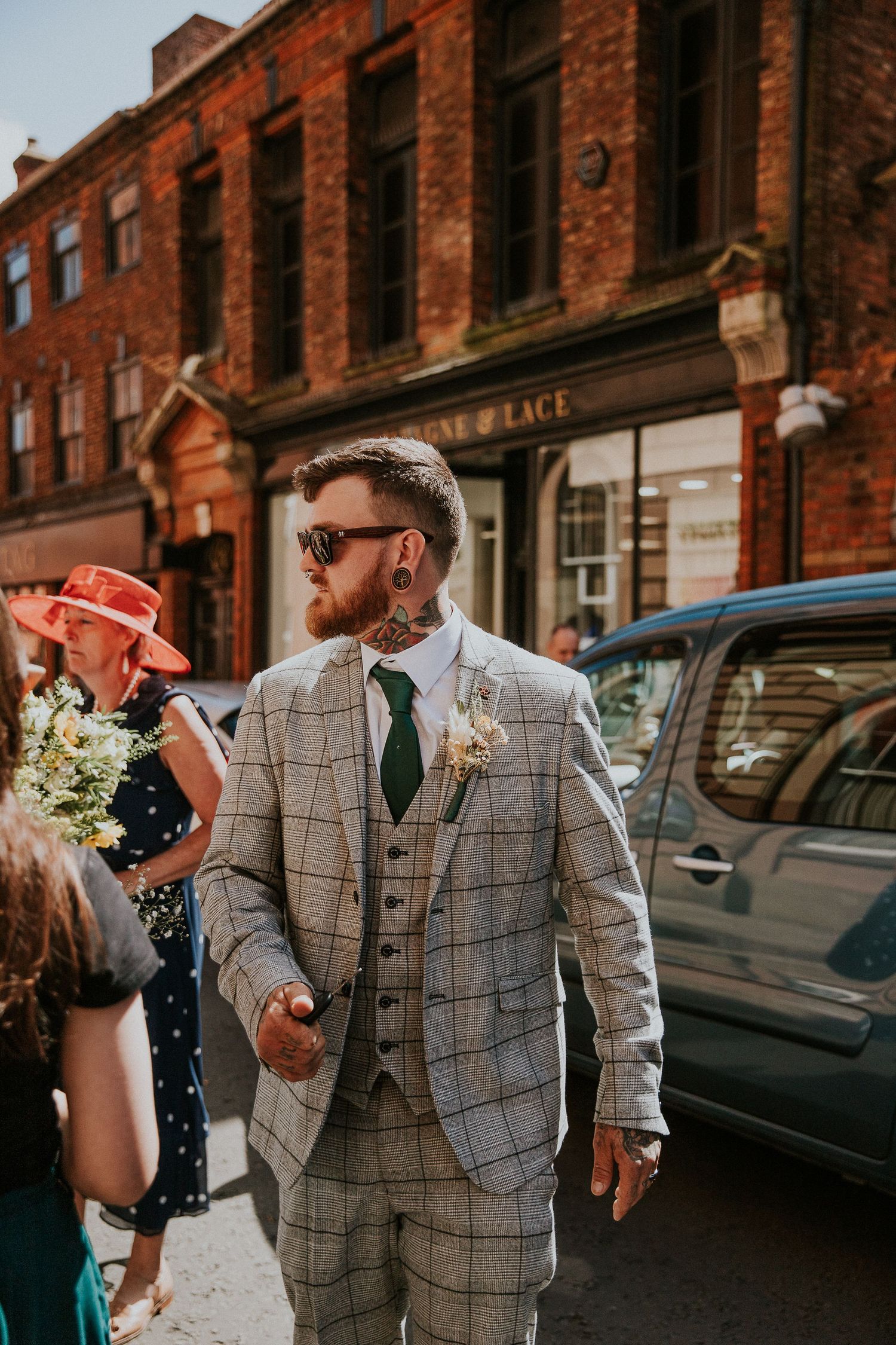 Groom in checkered suit outside brick building in urban setting.