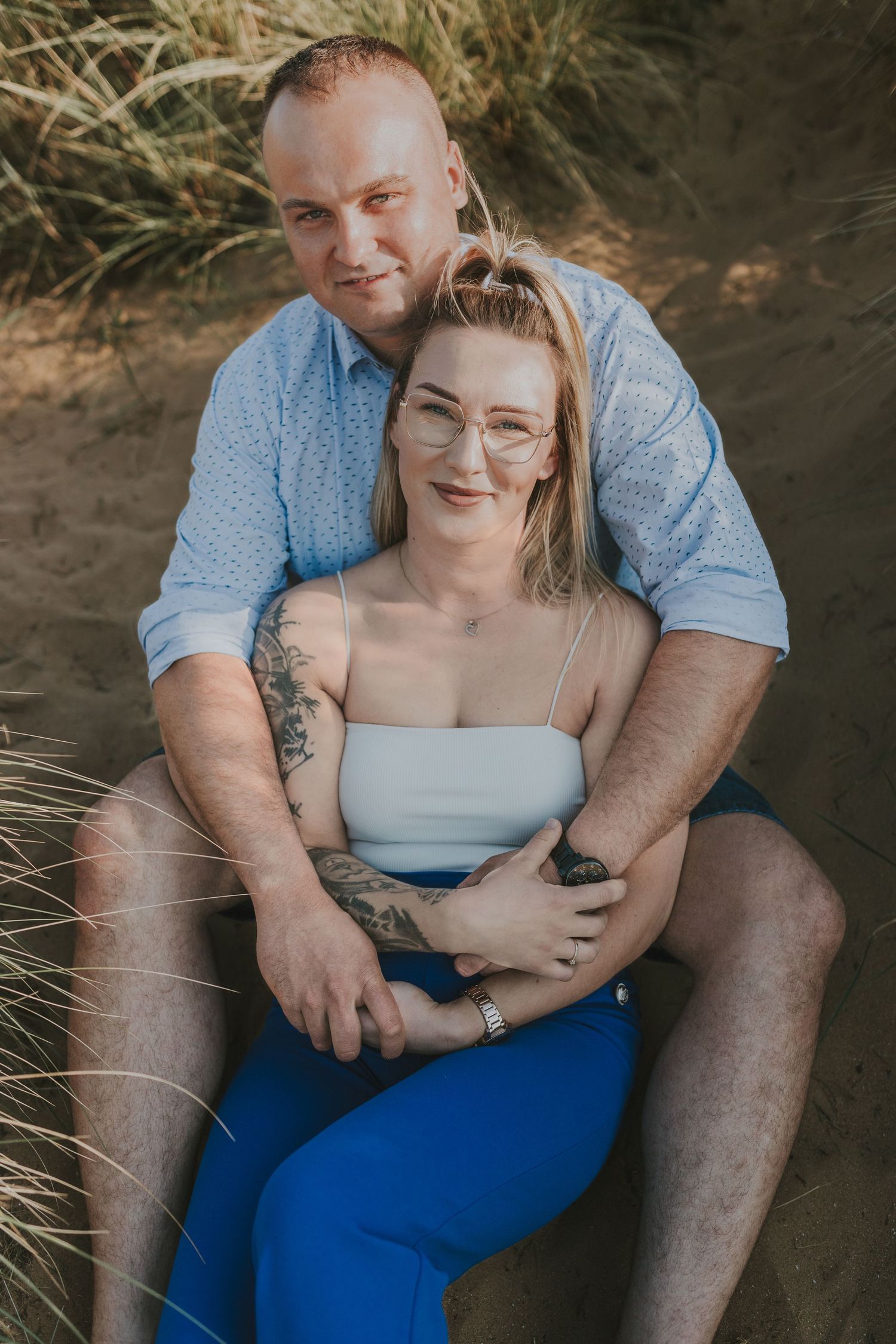 Couple sitting together on sandy beach during sunset engagement photoshoot.
