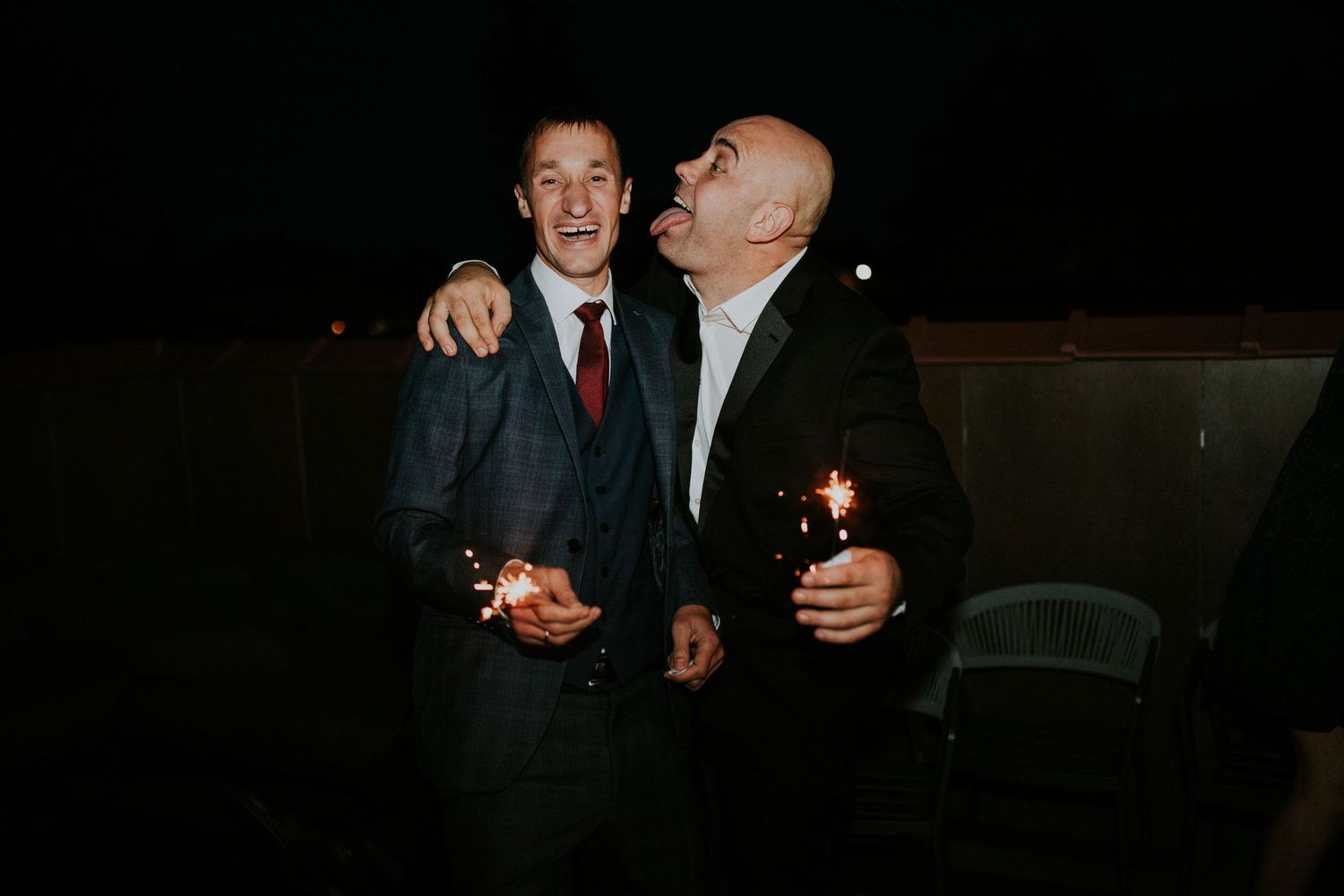 Two wedding guests sharing drinks and laughter during nighttime reception.