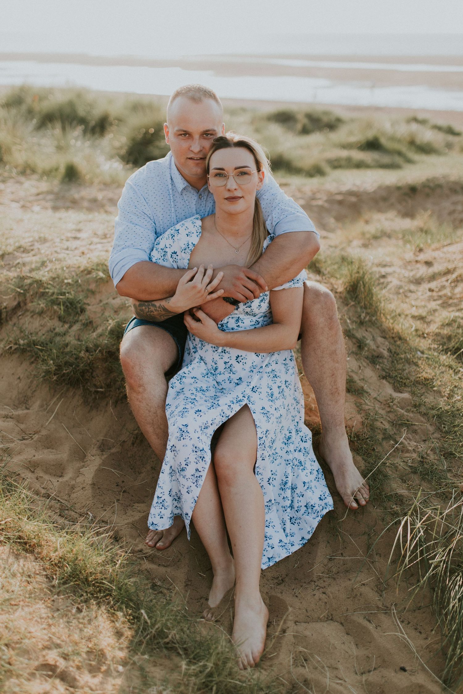 Intimate beachside portrait of couple sitting together on sandy dune.