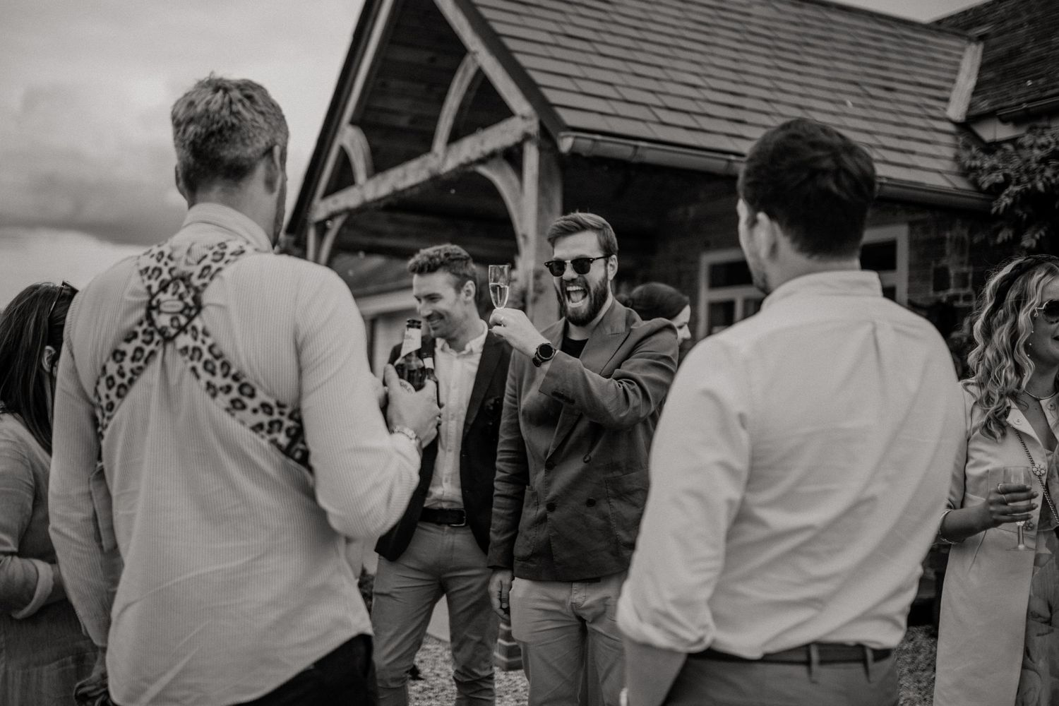 Groomsmen gather for casual black and white moment outside rustic venue.