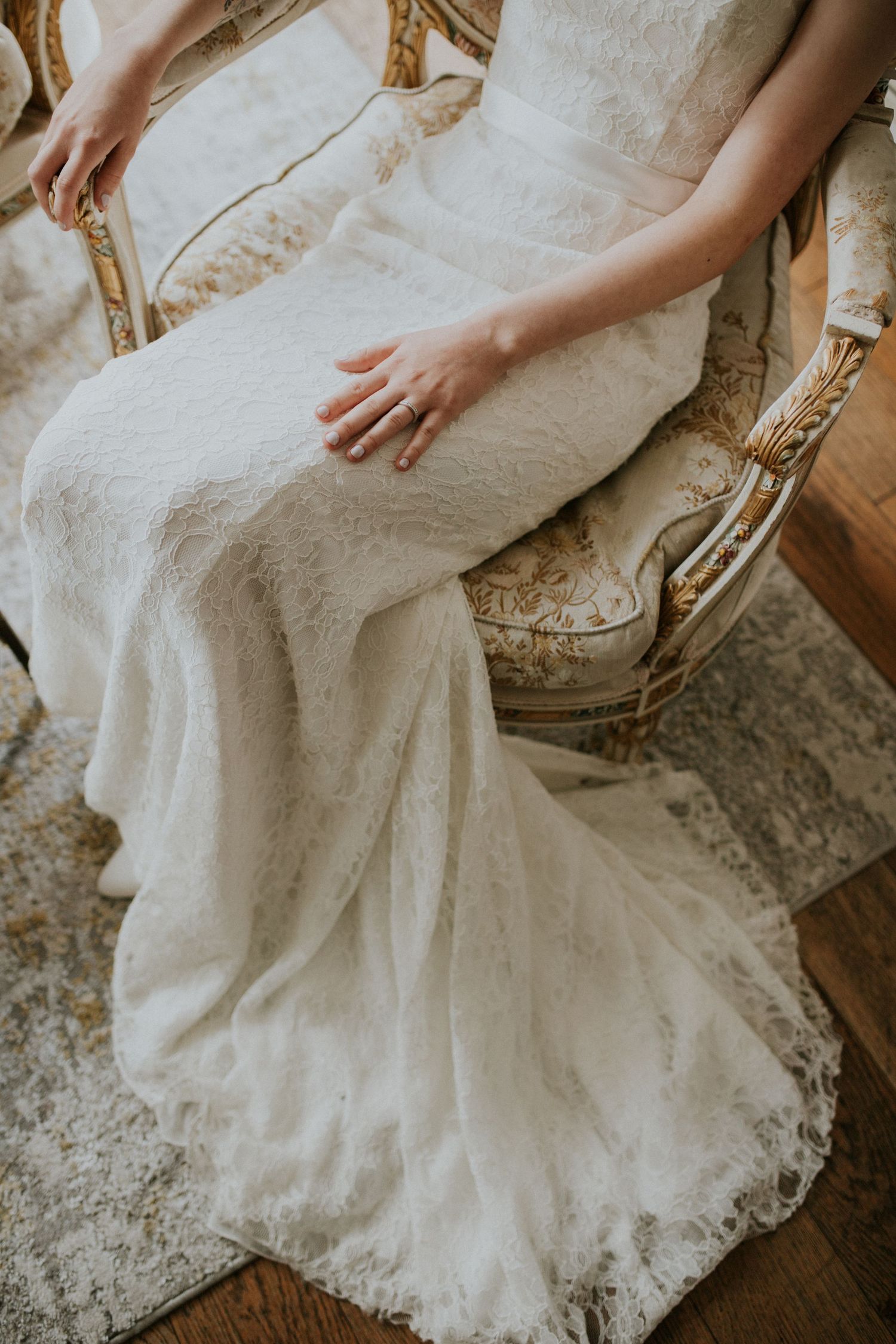 Detail shot of lace wedding dress train flowing gracefully across antique furniture.