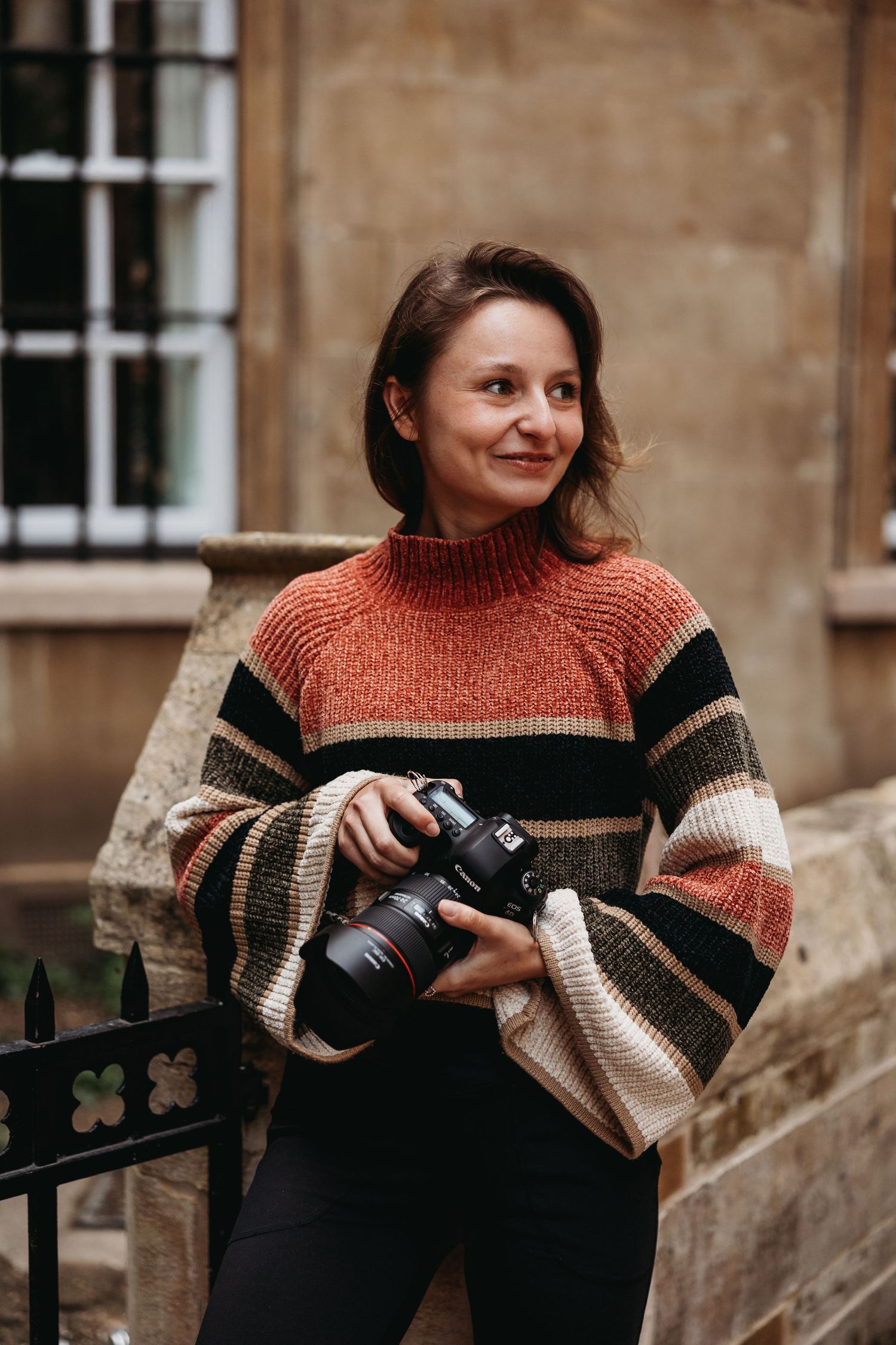 Photographer in striped sweater works with camera equipment against stone building backdrop.
