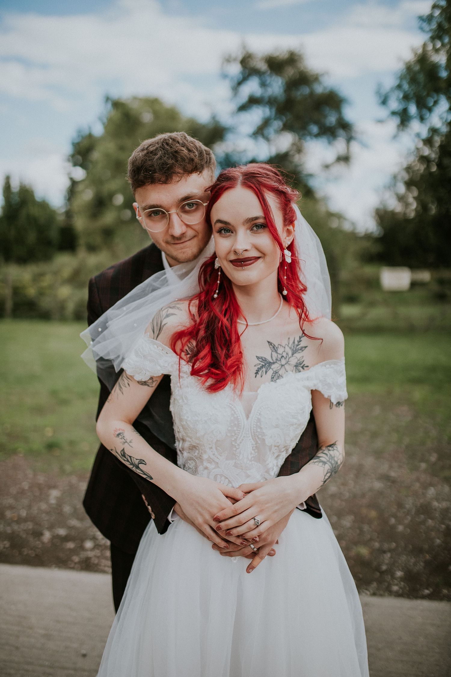 Bride with vibrant red hair in white wedding dress embraced by groom in outdoor portrait.