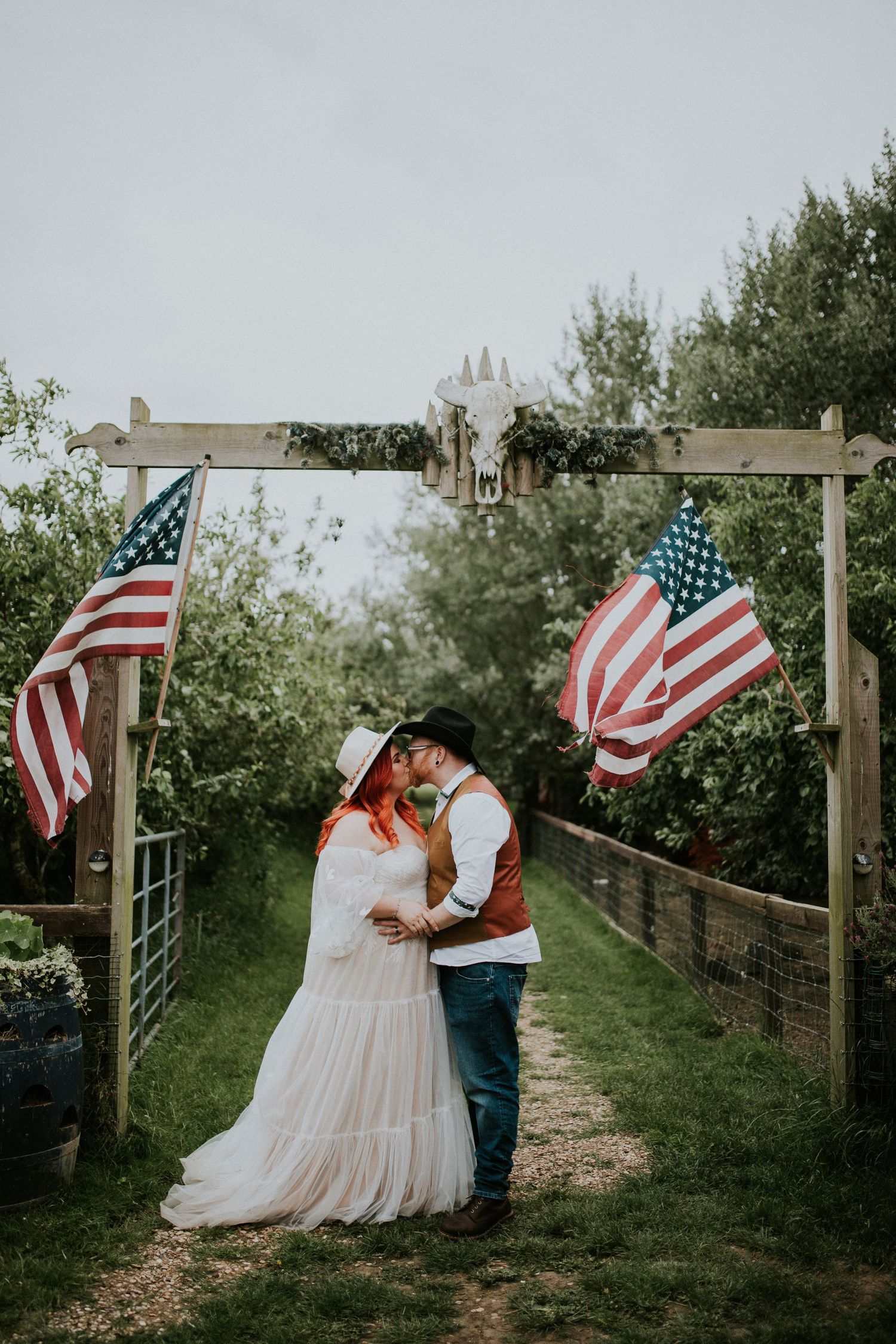 Romantic outdoor photoshoot with American flags along a wooden fence path.