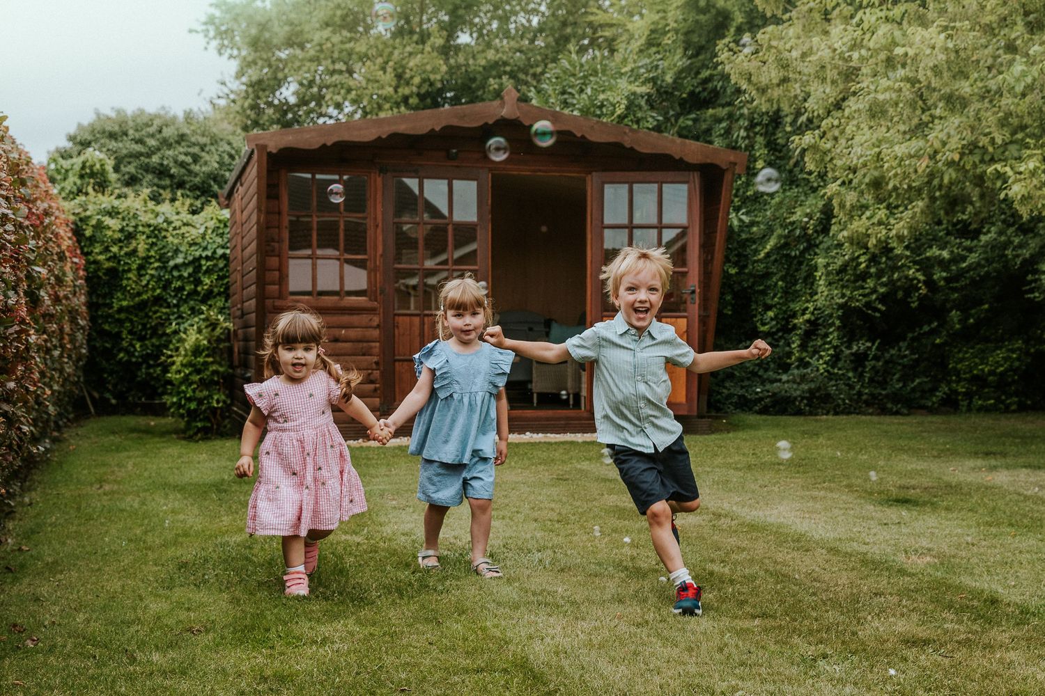 Children run and play together on green grass near wooden cabins.