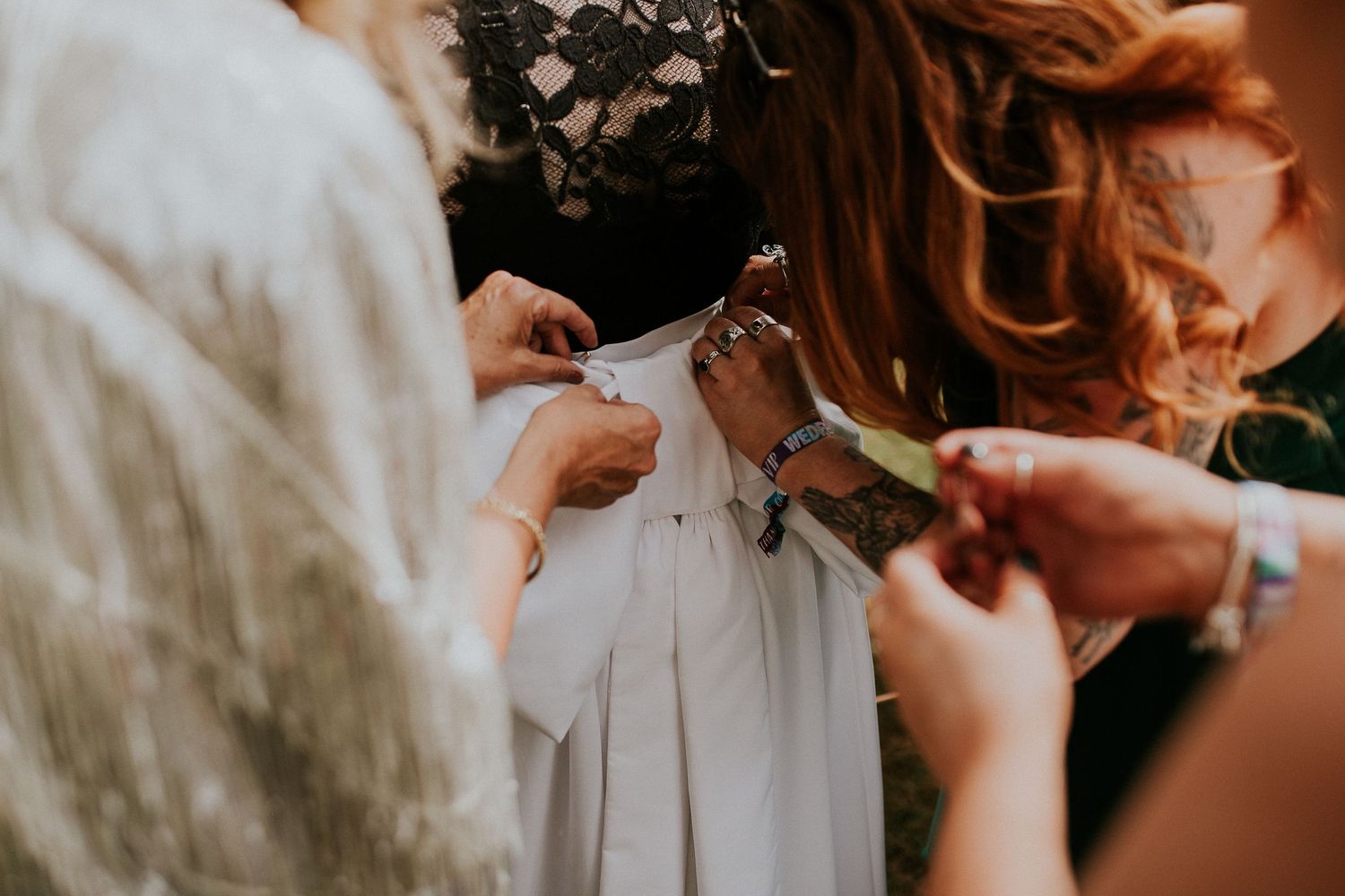 Close-up shot of hands working together to prepare a white wedding dress.