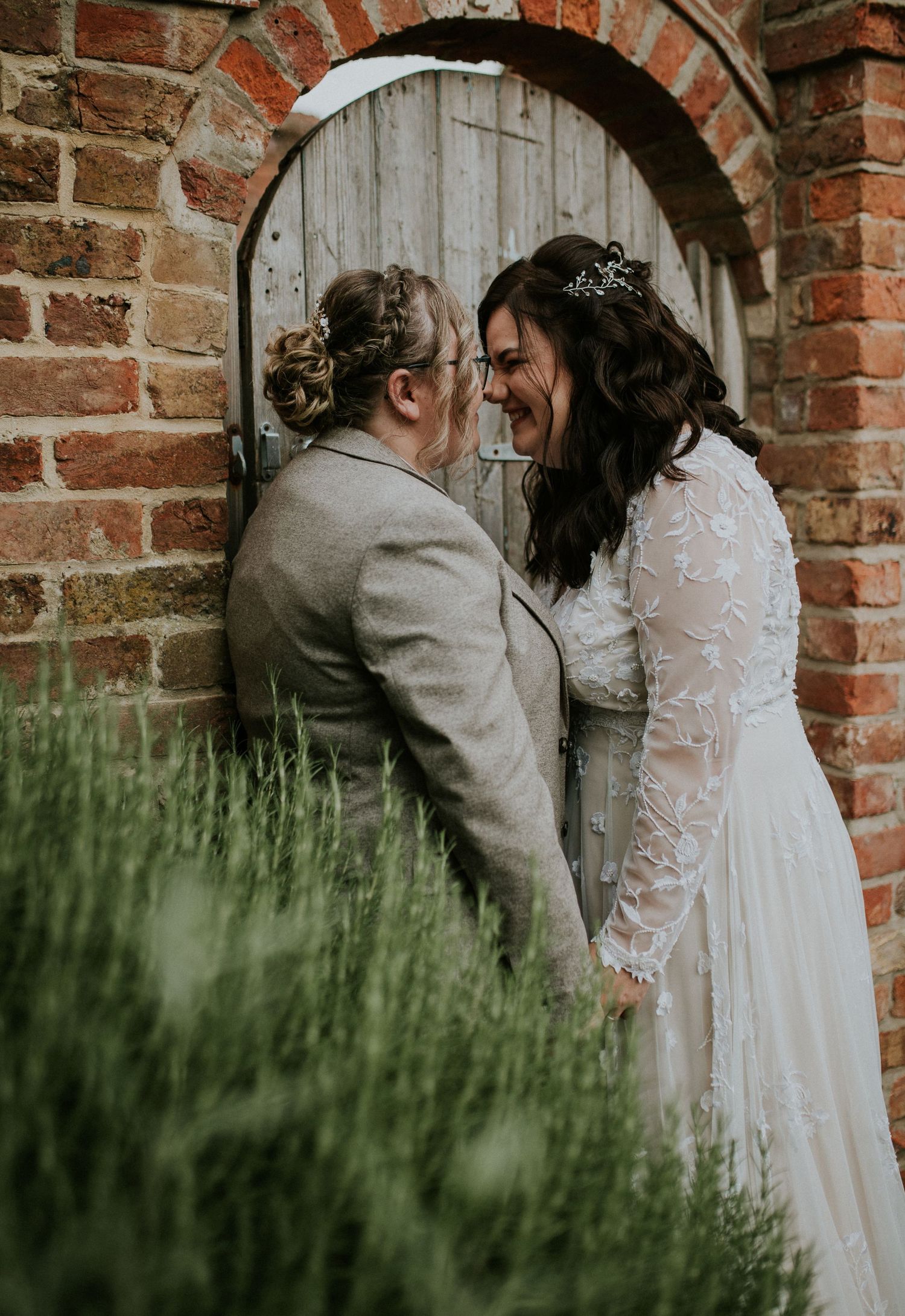 Two people share an intimate moment against a rustic brick archway and wooden door.