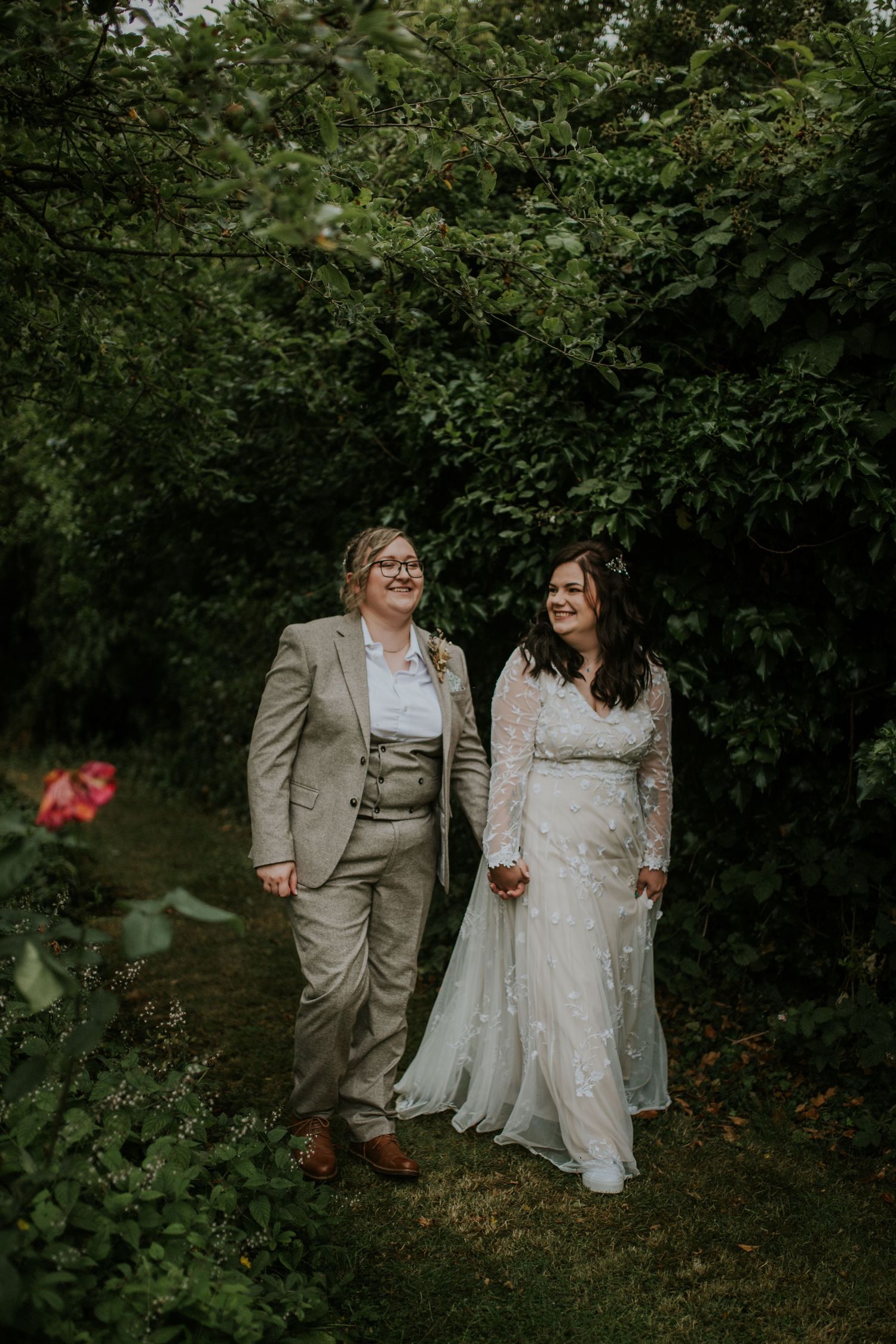 Wedding couple walking through a garden path with green foliage and natural lighting.