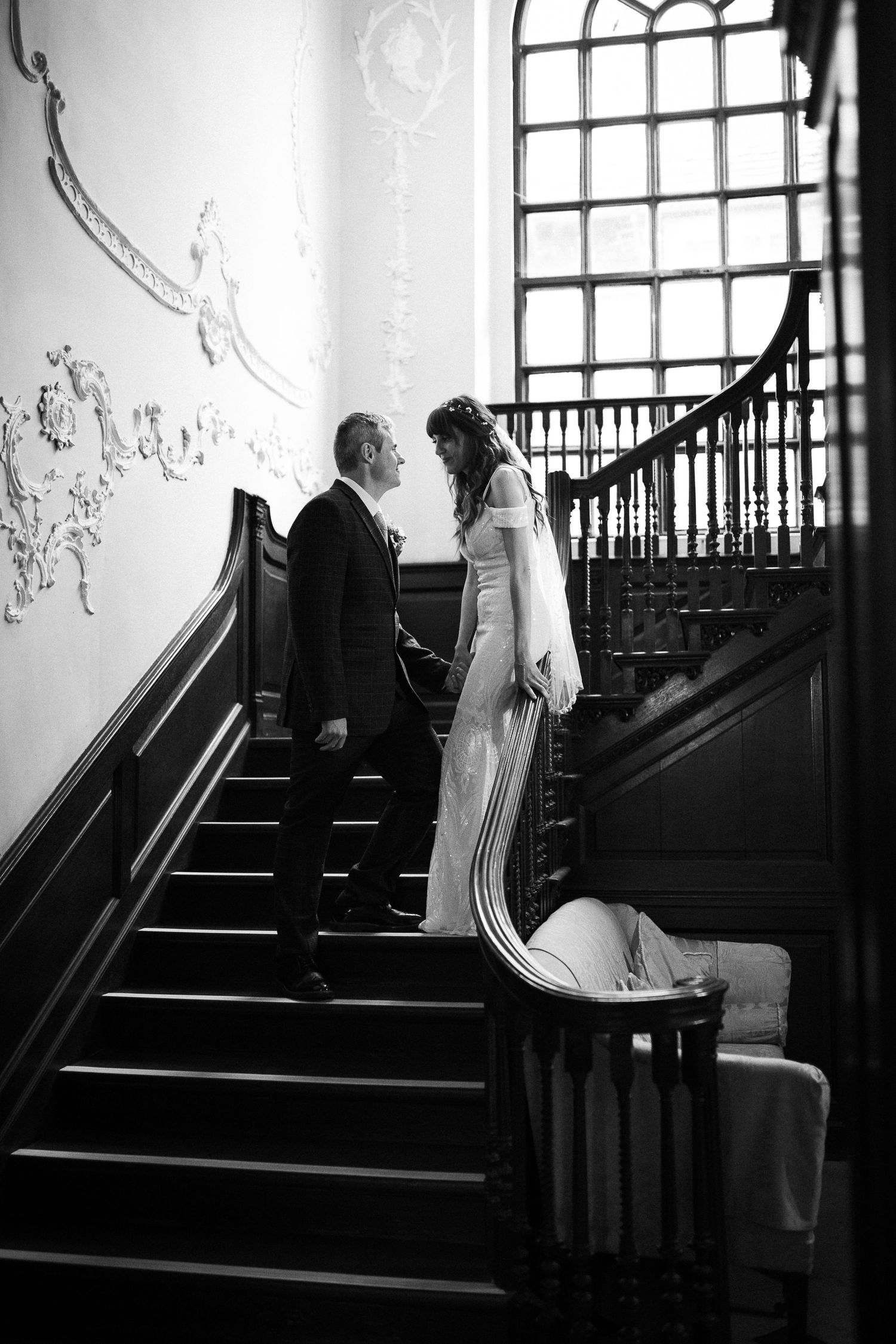 Black and white photo of couple on grand staircase with ornate wall details.