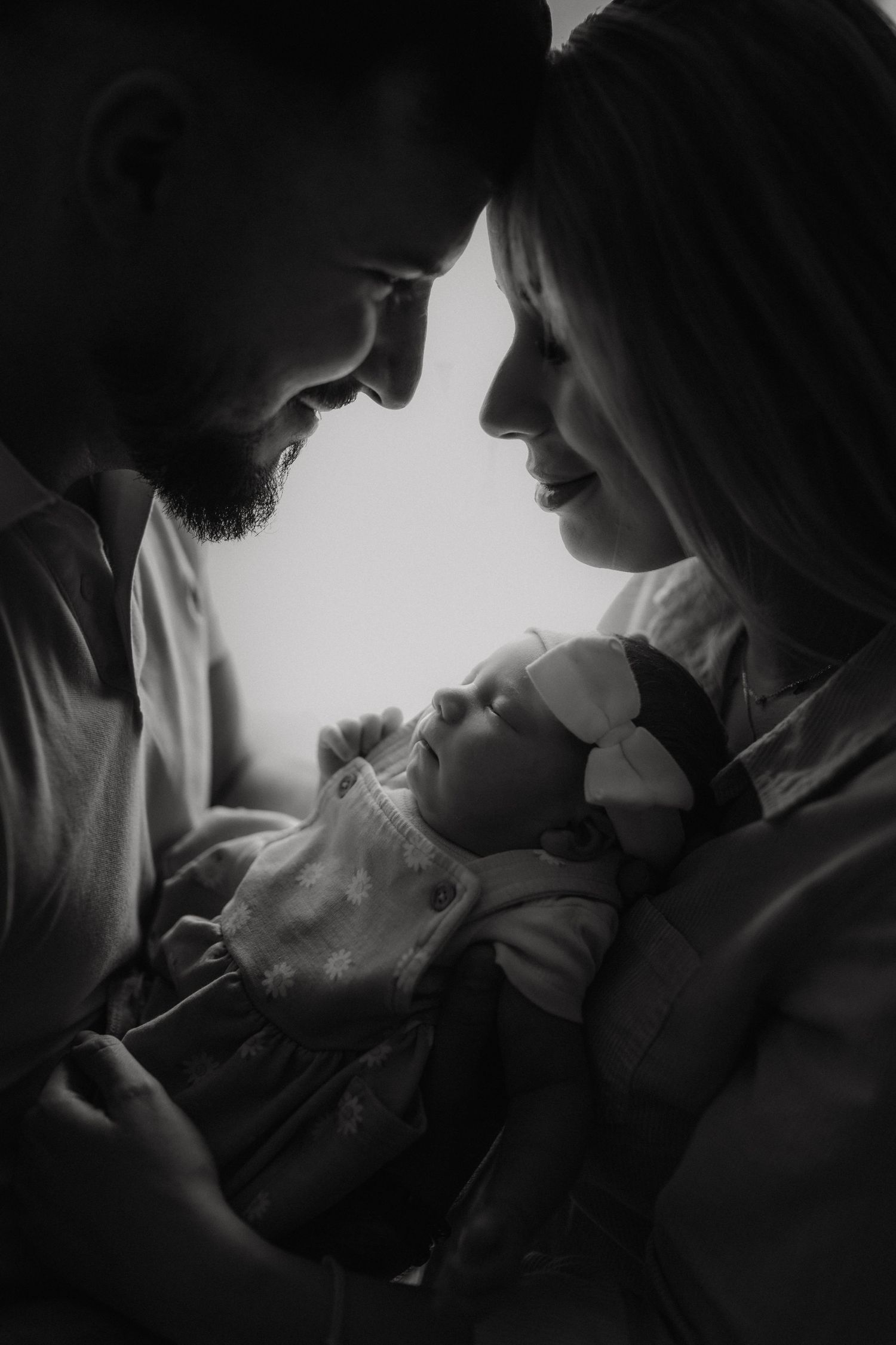 Intimate black and white portrait of parents gazing at their newborn baby.