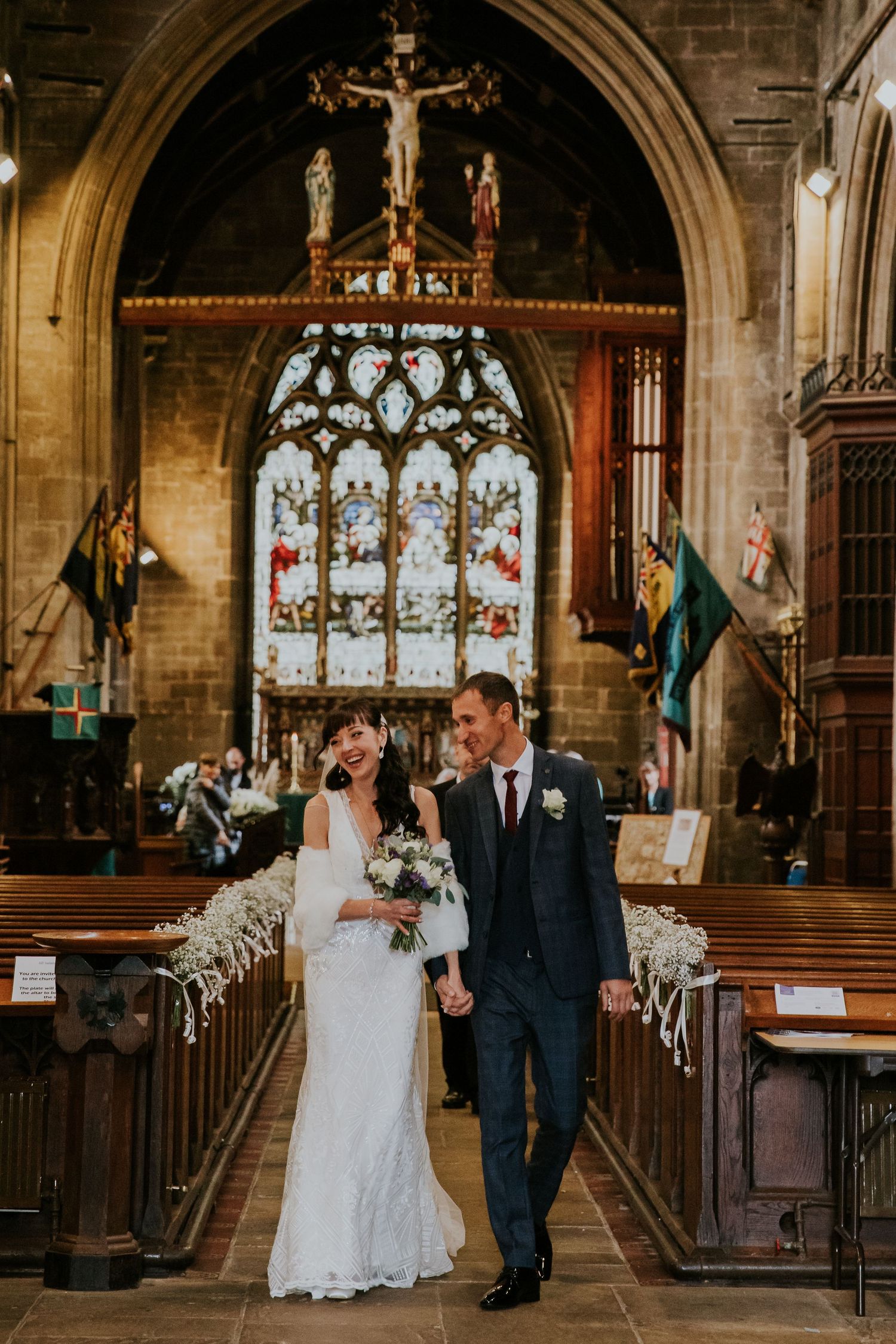 Newlyweds walk through ornate church interior with gothic architecture and stained glass.