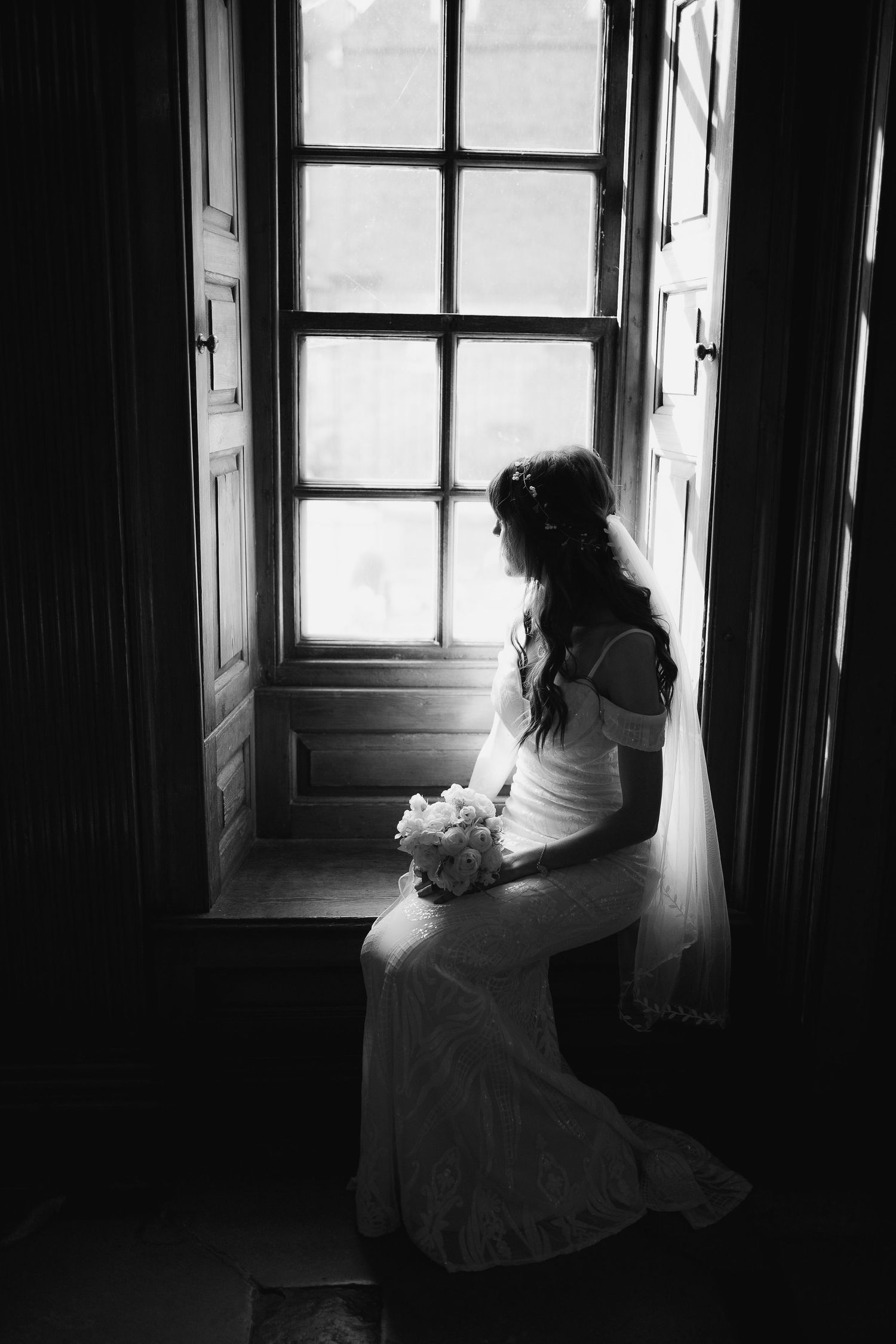 Black and white artistic wedding photos of a bride seated by a window creating a dramatic silhouette effect.