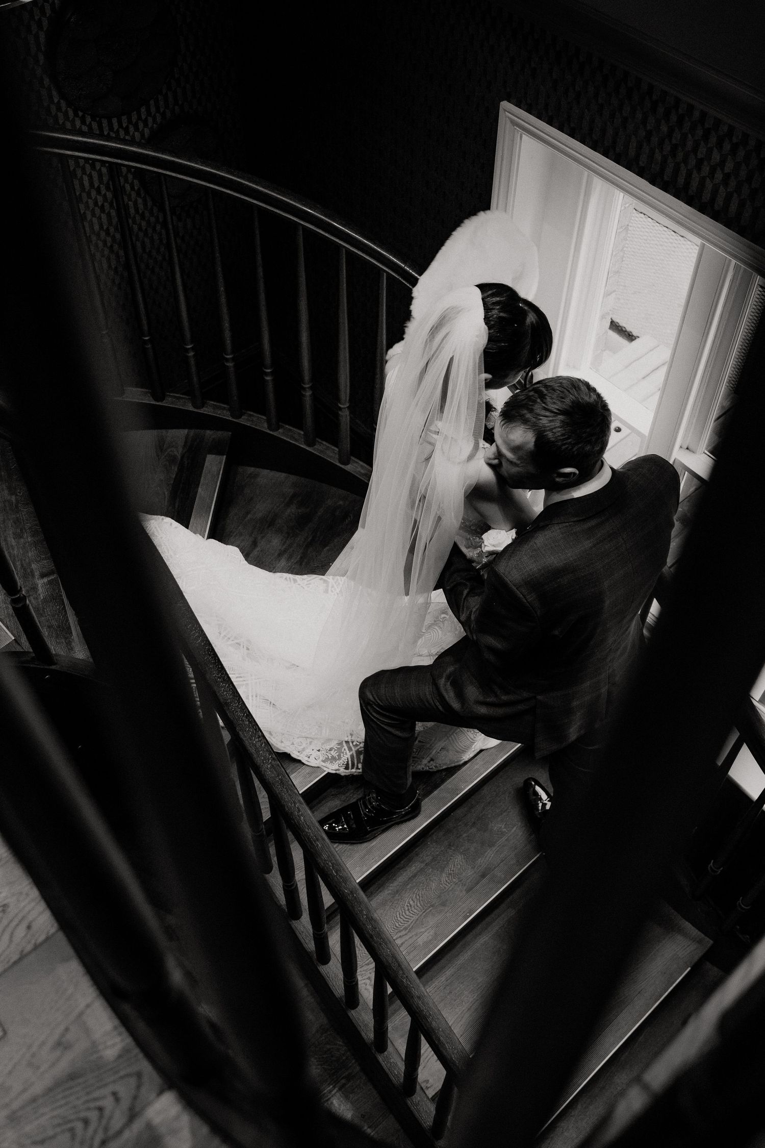 A moody black and white photo of newlyweds embracing on vintage spiral stairs.