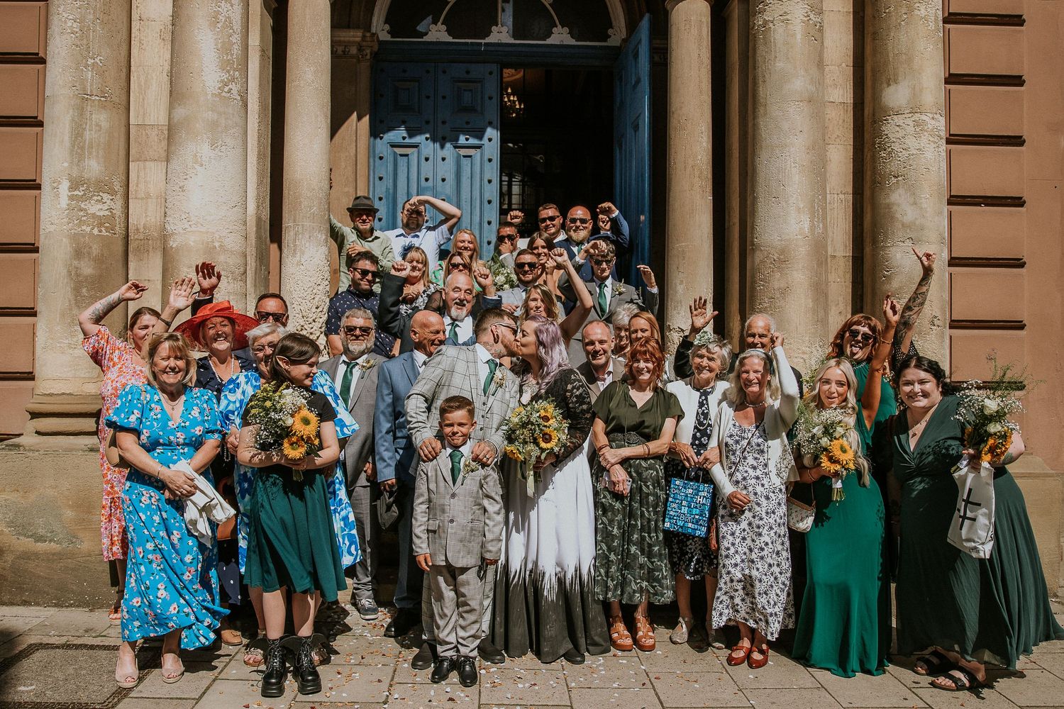 Large group wedding photo with guests celebrating on historic building steps.