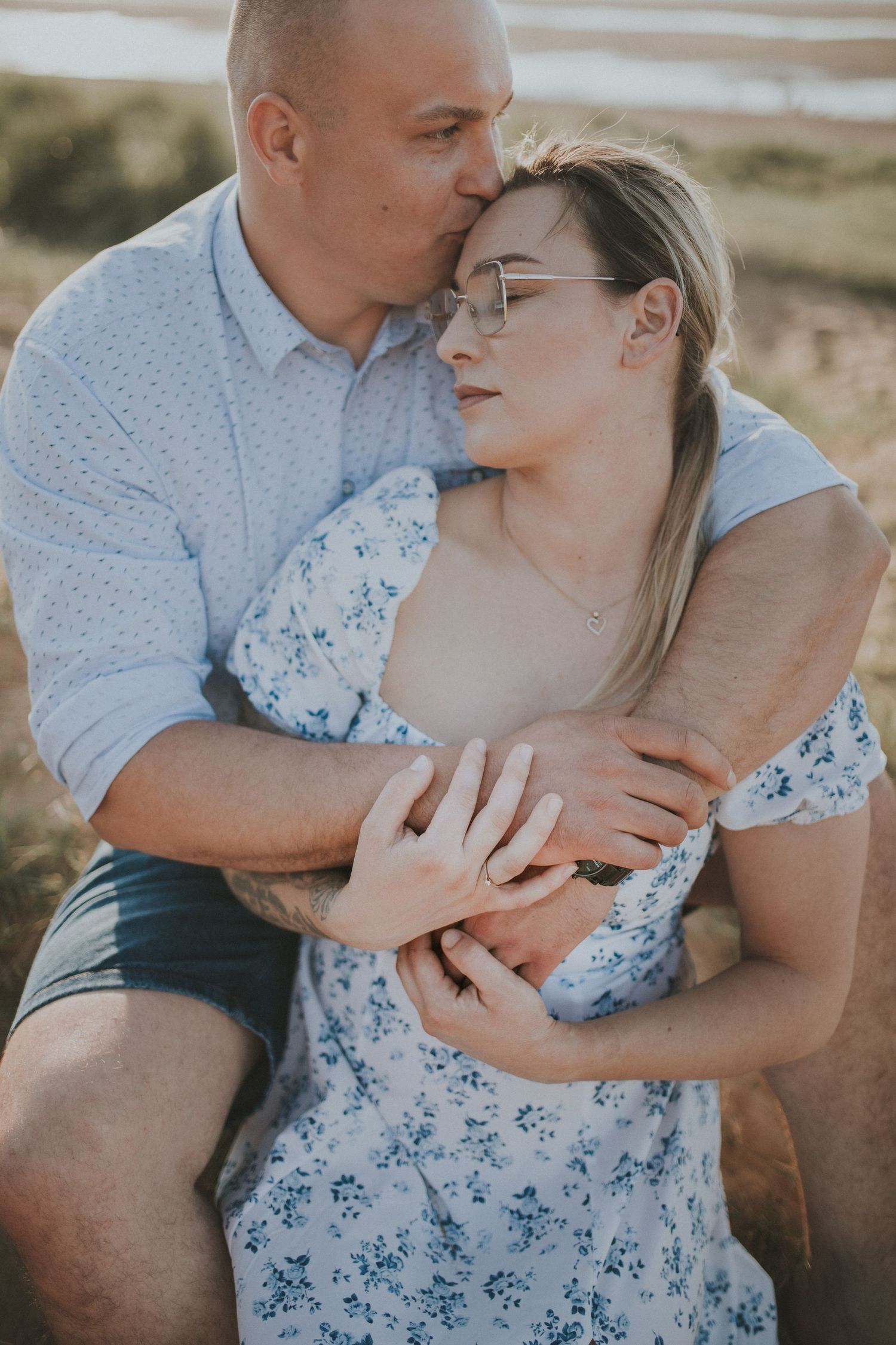 Tender moment between couple sharing embrace on coastal hillside at sunset.