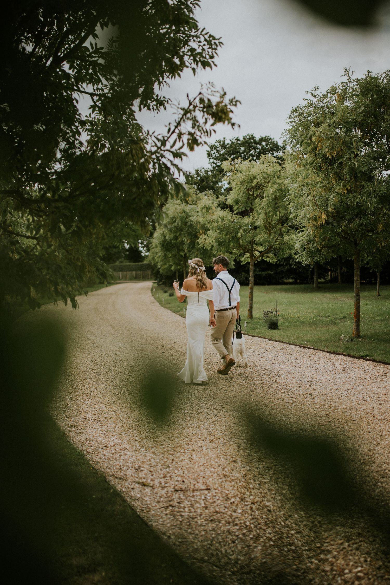 Couple walking along a gravel path surrounded by lush green trees during an intimate outdoor wedding.