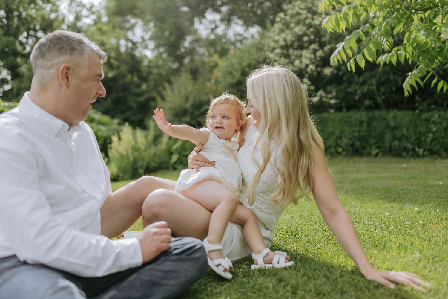 Family sharing tender moments together on sunny lawn with trees in background.