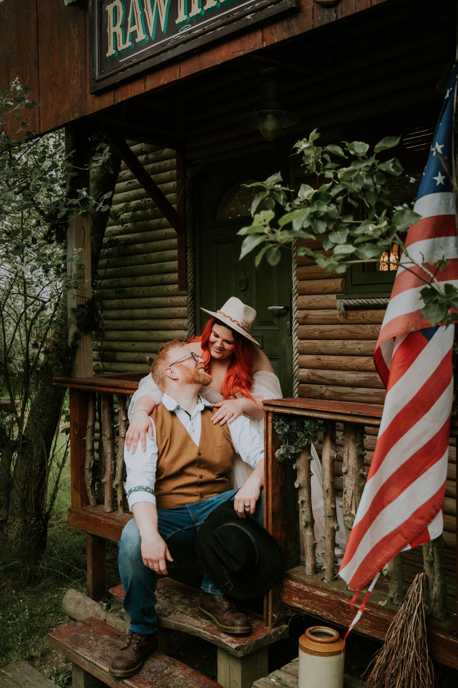 Rustic log cabin porch decorated with American flags and vintage western signs.